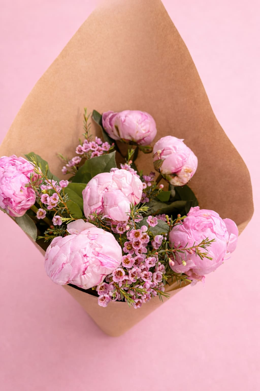Pink peonies wrapped in brown paper with small pink filler flowers