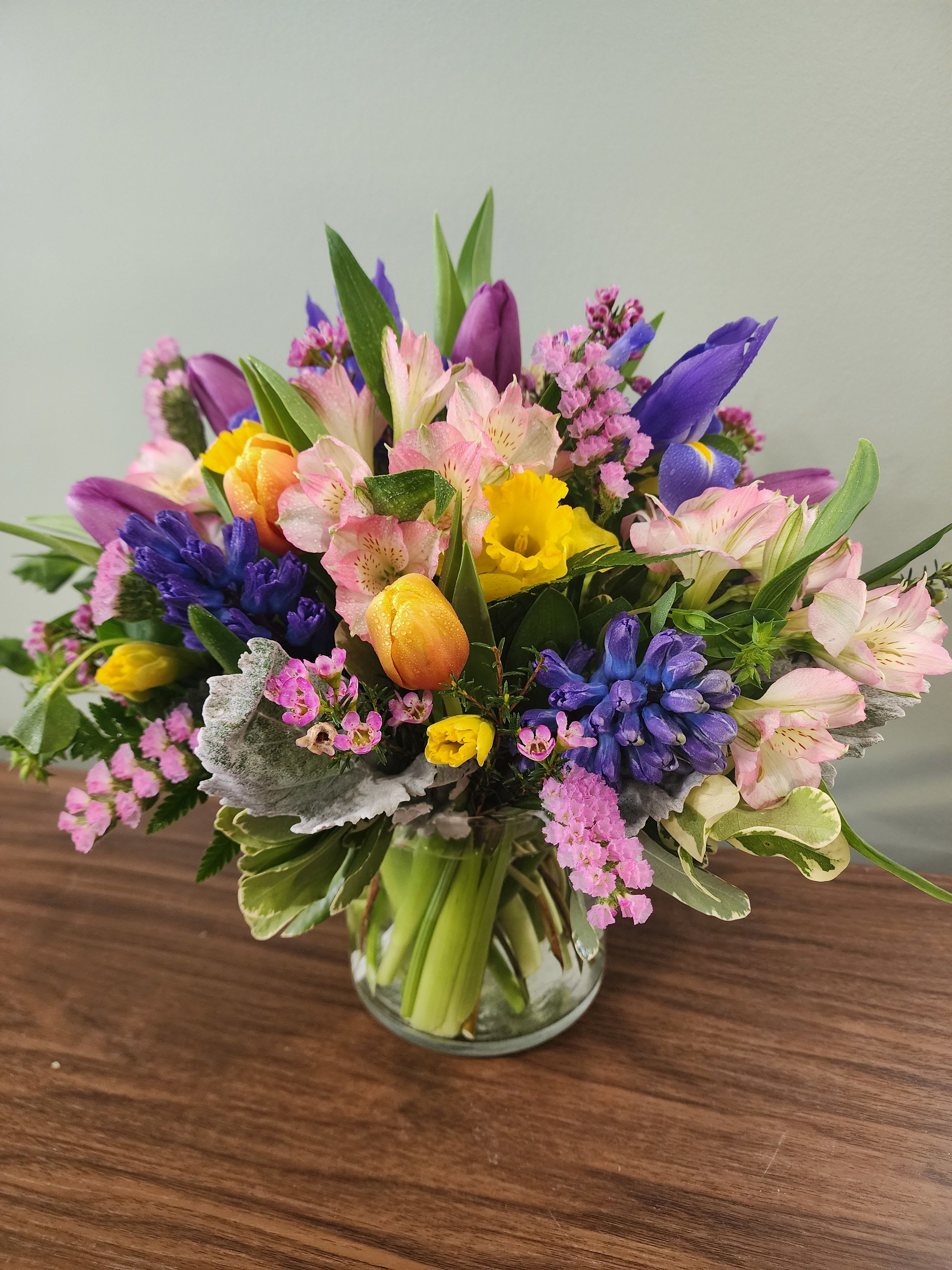 Springtime Serenade by MG Florist  - Spring Serenade – Fresh Spring Flower Arrangement by The Magic Garden Florist – Same Day Delivery in Rochester, NY  Welcome the beauty of spring into your home or office with the Spring Serenade flower arrangement from The Magic Garden Florist. Designed in an elegant glass vase, this vibrant bouquet features lush mixed greens as a foundation for seasonal favorites, including fragrant hyacinths, colorful tulips, elegant iris, cheerful daffodils, delicate statice, and bright alstroemeria. Each bloom is thoughtfully arranged to create a harmonious display that evokes the freshness, color, and joy of spring.  Perfect for spring centerpieces, birthday gifts, Easter décor, or simply to brighten someone’s day, Spring Serenade is available for same day flower delivery in Rochester, NY. Celebrate the season with a fresh, colorful bouquet that captures the essence of springtime. Flowers and colors may vary by availability.
