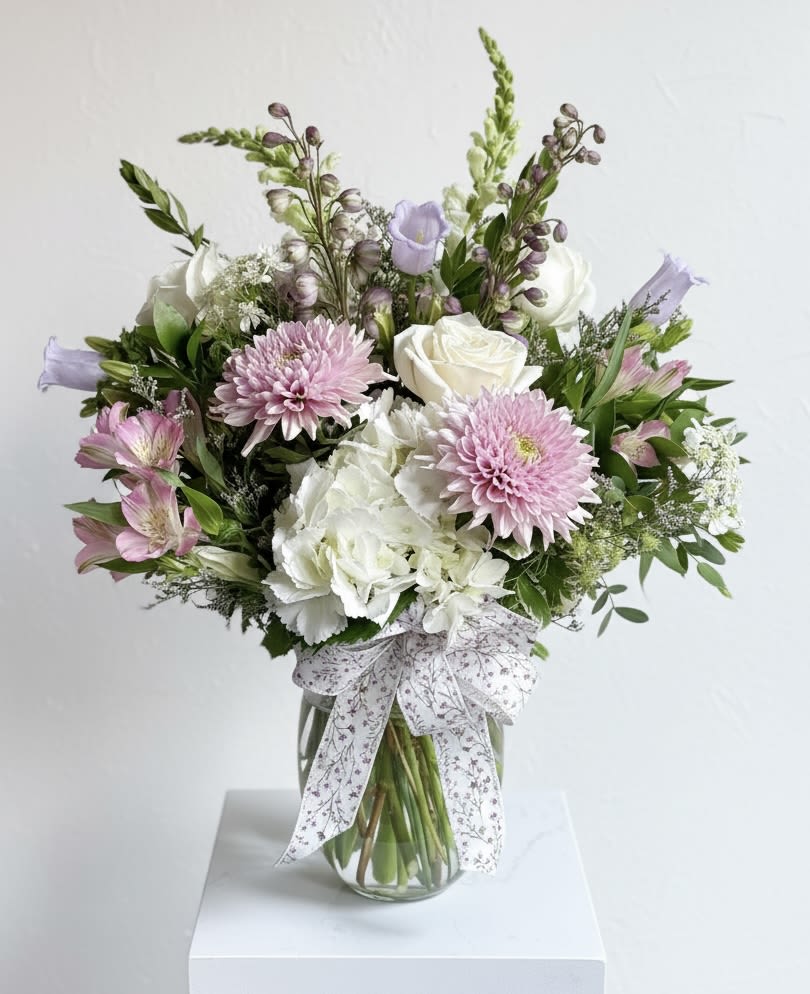 Soft Colored Seasonal Mix-Size large  - A clear glass vase, filled with pinkish lavender cremons, lavender hybrid delphinium, white roses, lavender companula, pink alstroemeria and white snapdragons. Soft and pretty! 