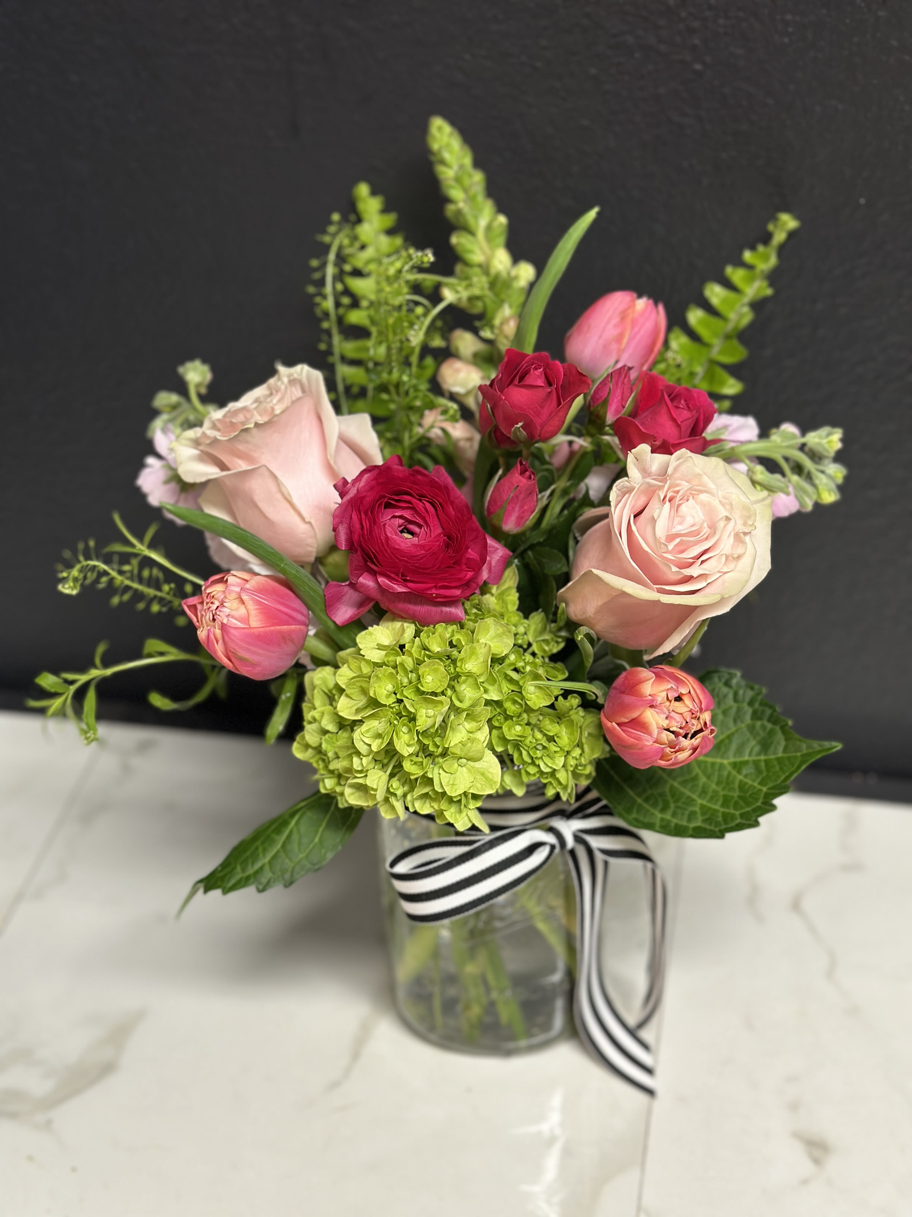 Pink Bloom Jar - A pretty seasonal garden mix in shades of soft to hot pink. Arranged in our clear glass bloom jar. Overall design is approximately 12" tall.  Floral varieties may vary but will be of similar quality and style.  