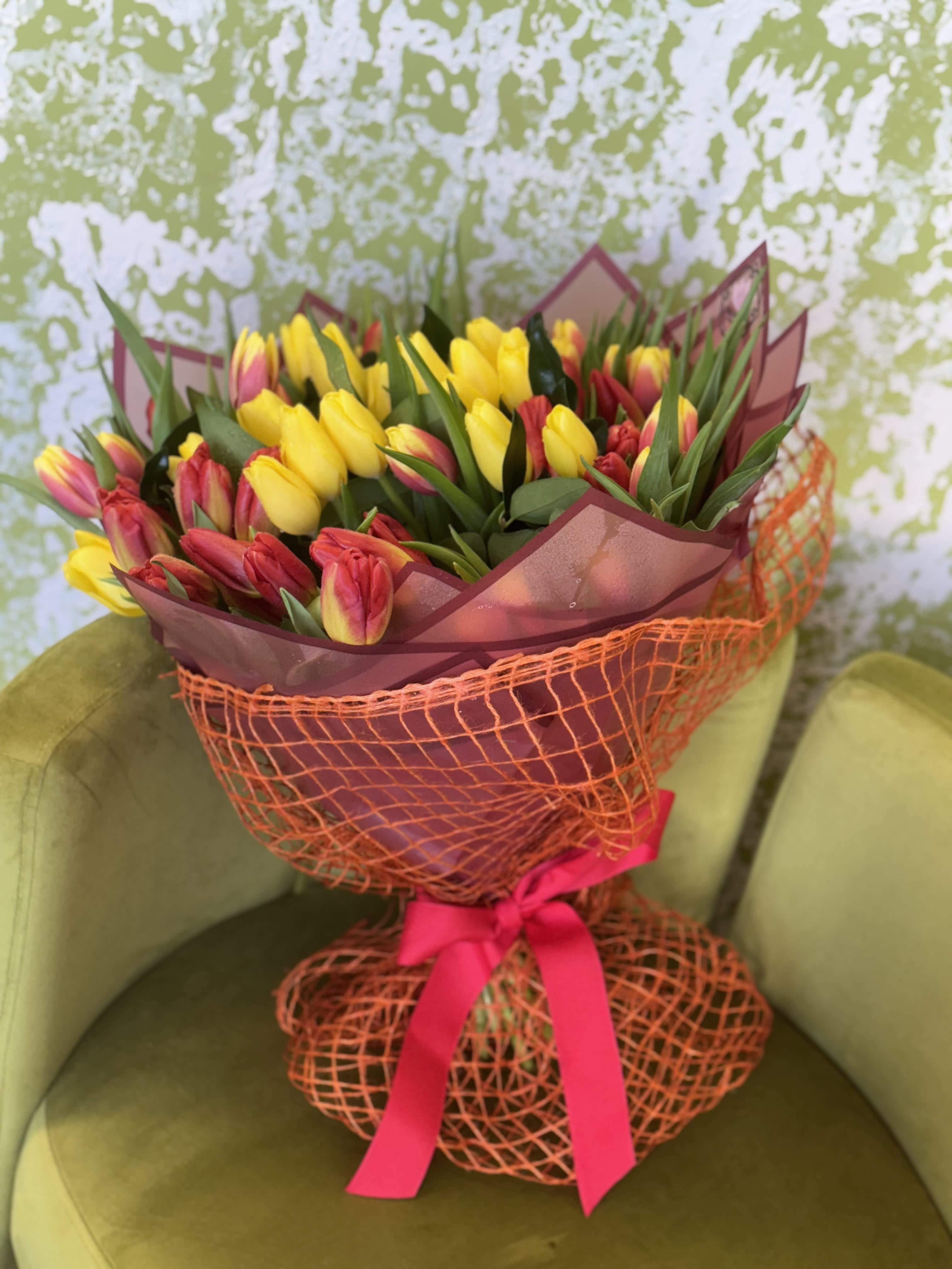 Bouquet of yellow and red tulips wrapped in orange mesh with a pink ribbon