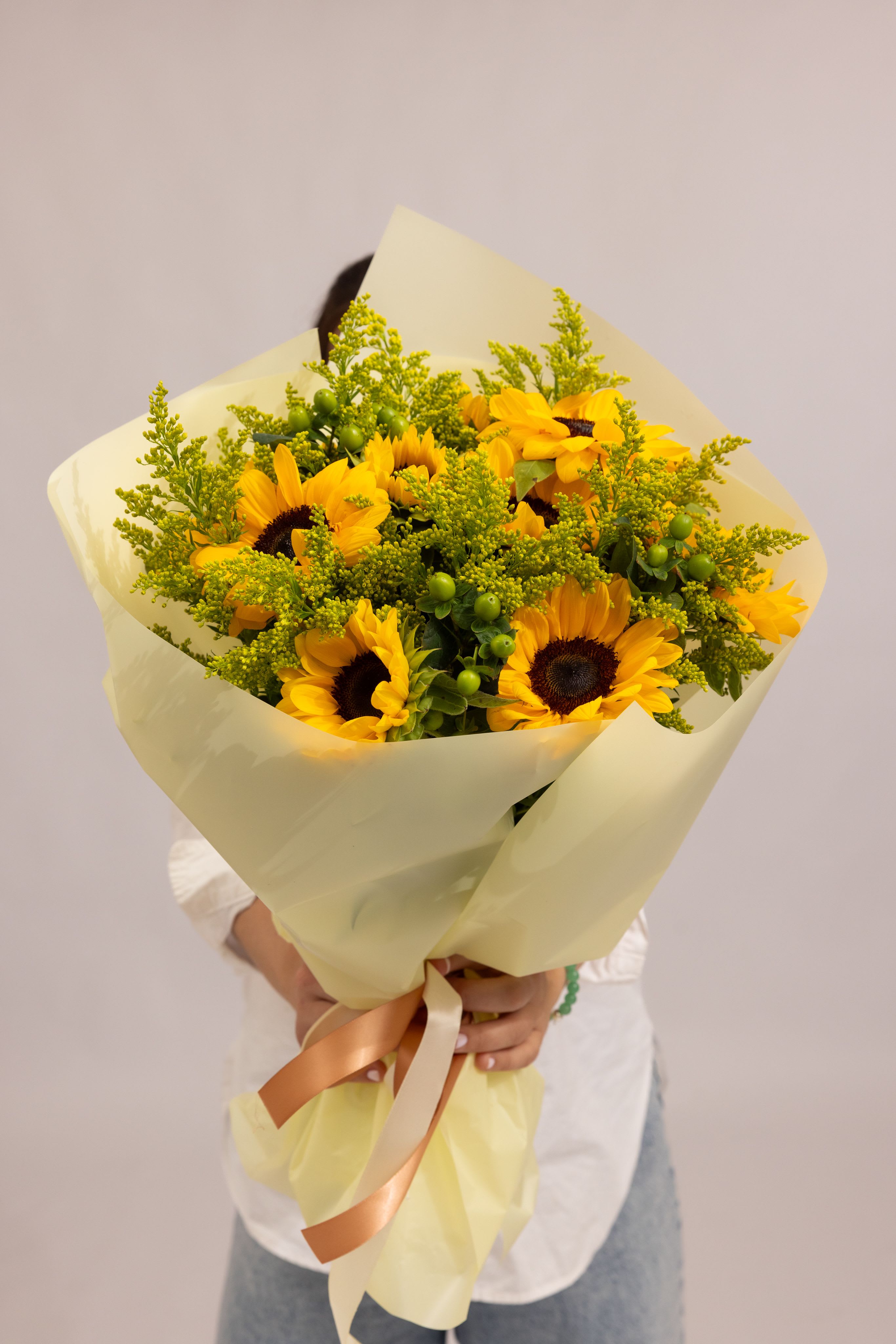 Sunlit Aura - A radiant bouquet featuring 9 vibrant sunflowers as the heart of the composition, complemented by fresh green berries and airy solidago. The rich yellow tones paired with soft greenery create a warm, uplifting arrangement that feels both natural and elegant. Designed to bring light, joy, and a touch of sunshine into any moment—perfect for celebrations or simply brightening someone’s day