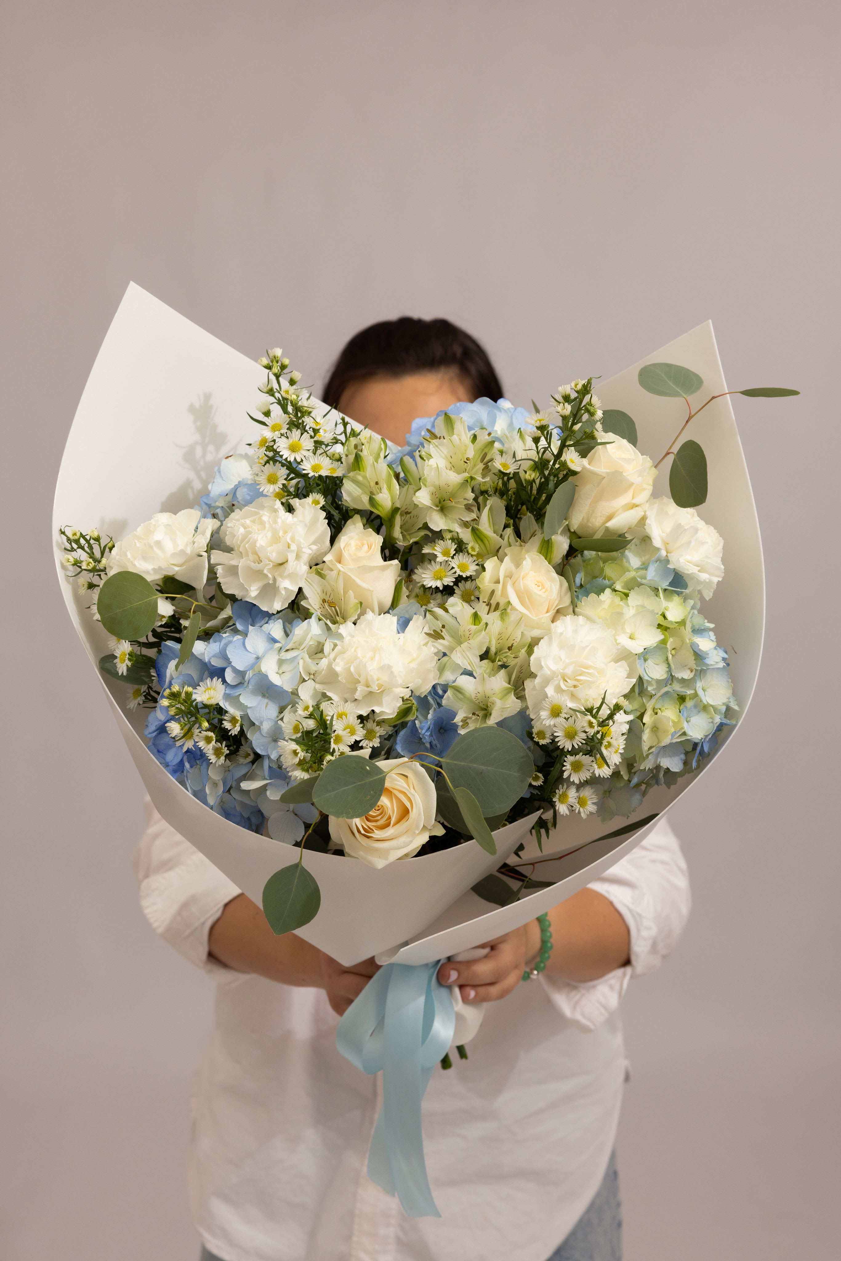 Sky Elegance - A delicate and airy bouquet in soft blue and white tones, featuring cream roses, white carnations, white alstroemeria, and clusters of Monte Casino, beautifully complemented by lush blue and white hydrangeas and fresh greenery. The gentle color palette and layered textures create a refined, cloud-like composition that feels calm, elegant, and effortlessly sophisticated. Designed to bring a sense of serenity and grace to any moment—perfect for meaningful occasions and timeless gifts