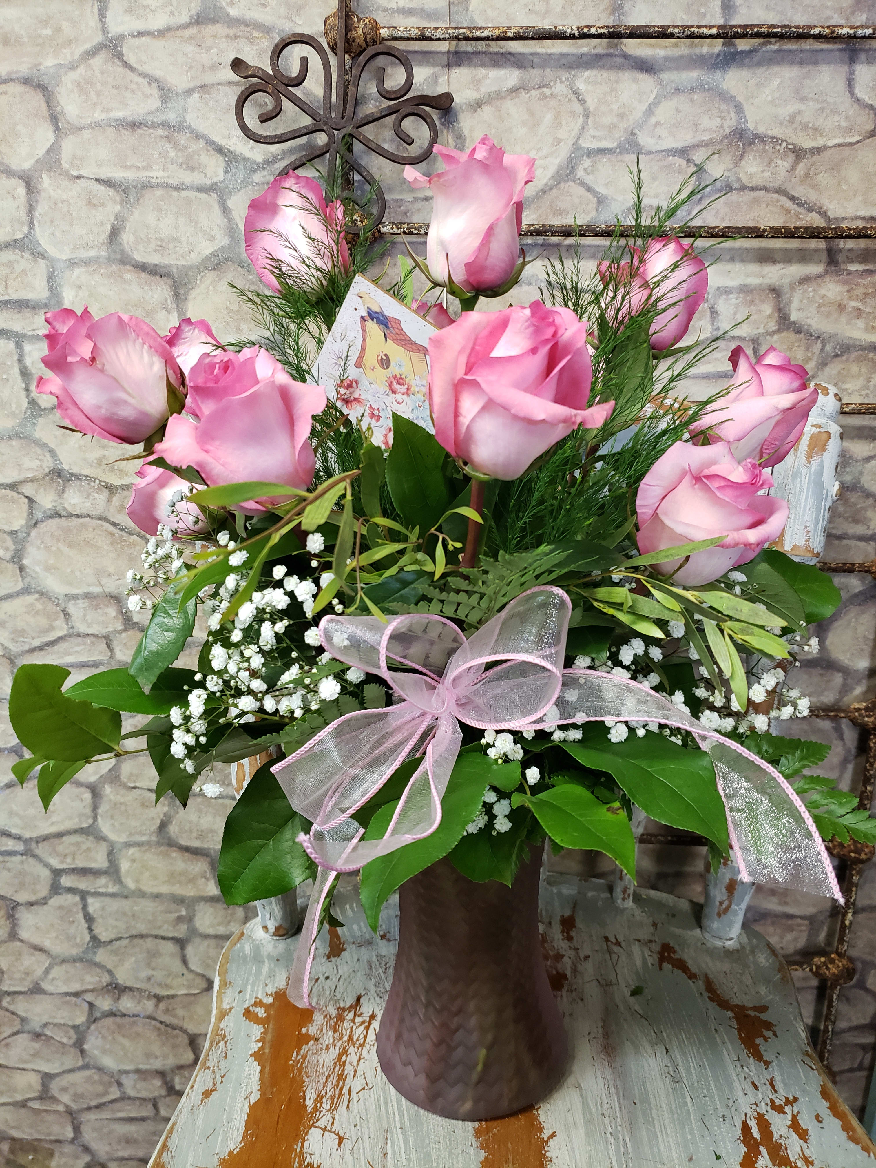 Arrangement of pink roses and white baby’s breath in a mauve glass vase with a pink ribbon bow.
