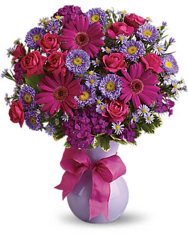 Bouquet of pink and purple flowers in a lavender vase with a ribbon