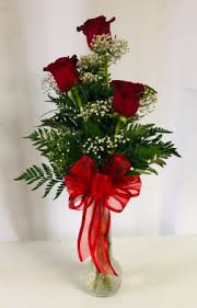 Red roses arranged in a clear vase with a large red bow