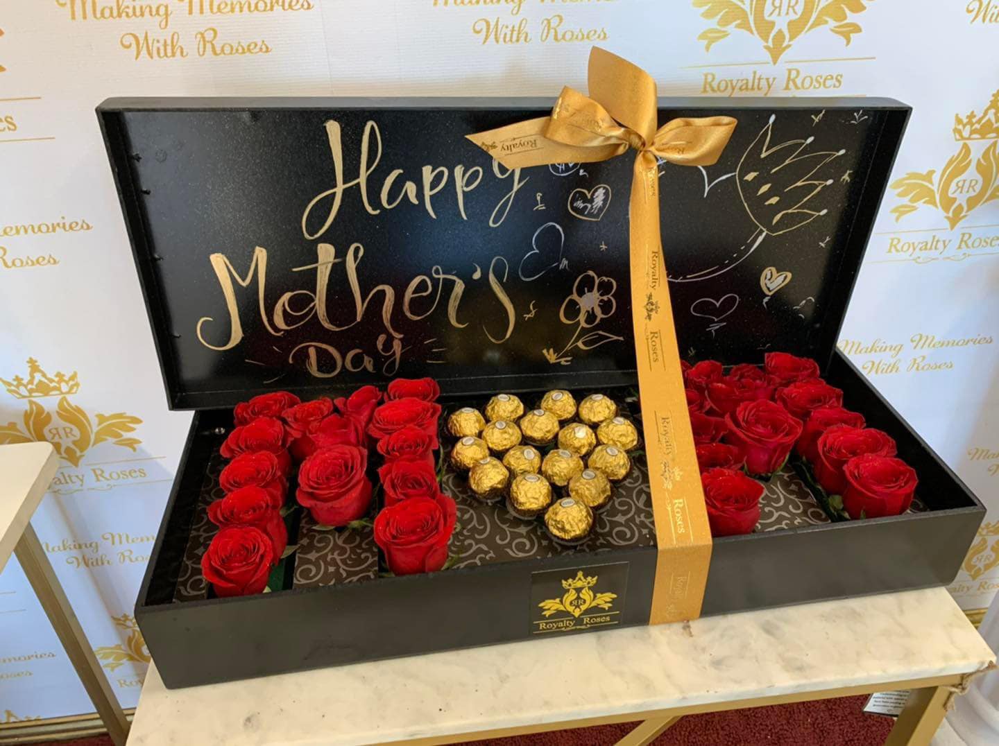 Black gift box with red roses and gold-wrapped chocolates for Mother's Day
