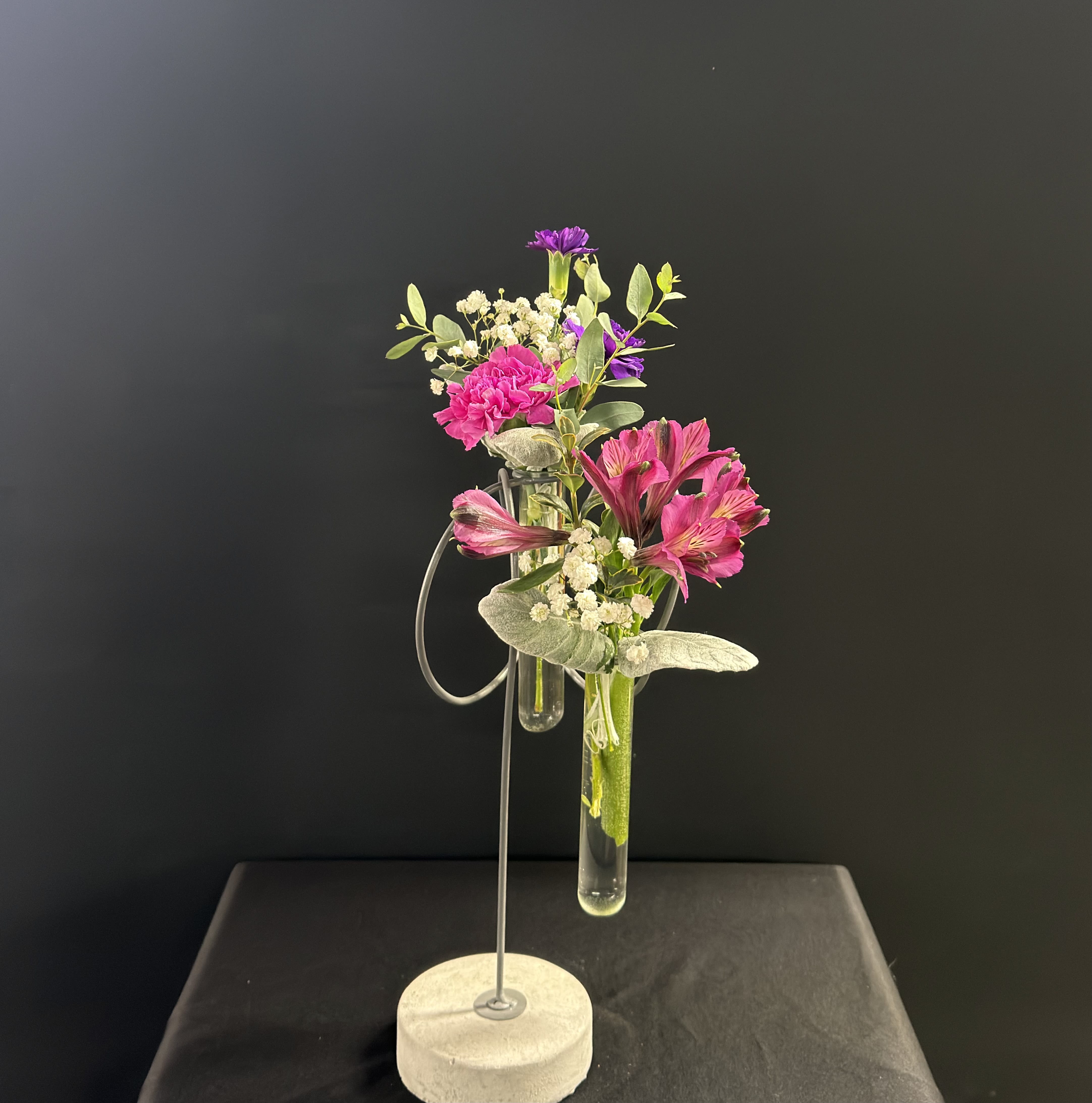 Pink and purple flowers arranged in hanging glass tubes on a metal stand
