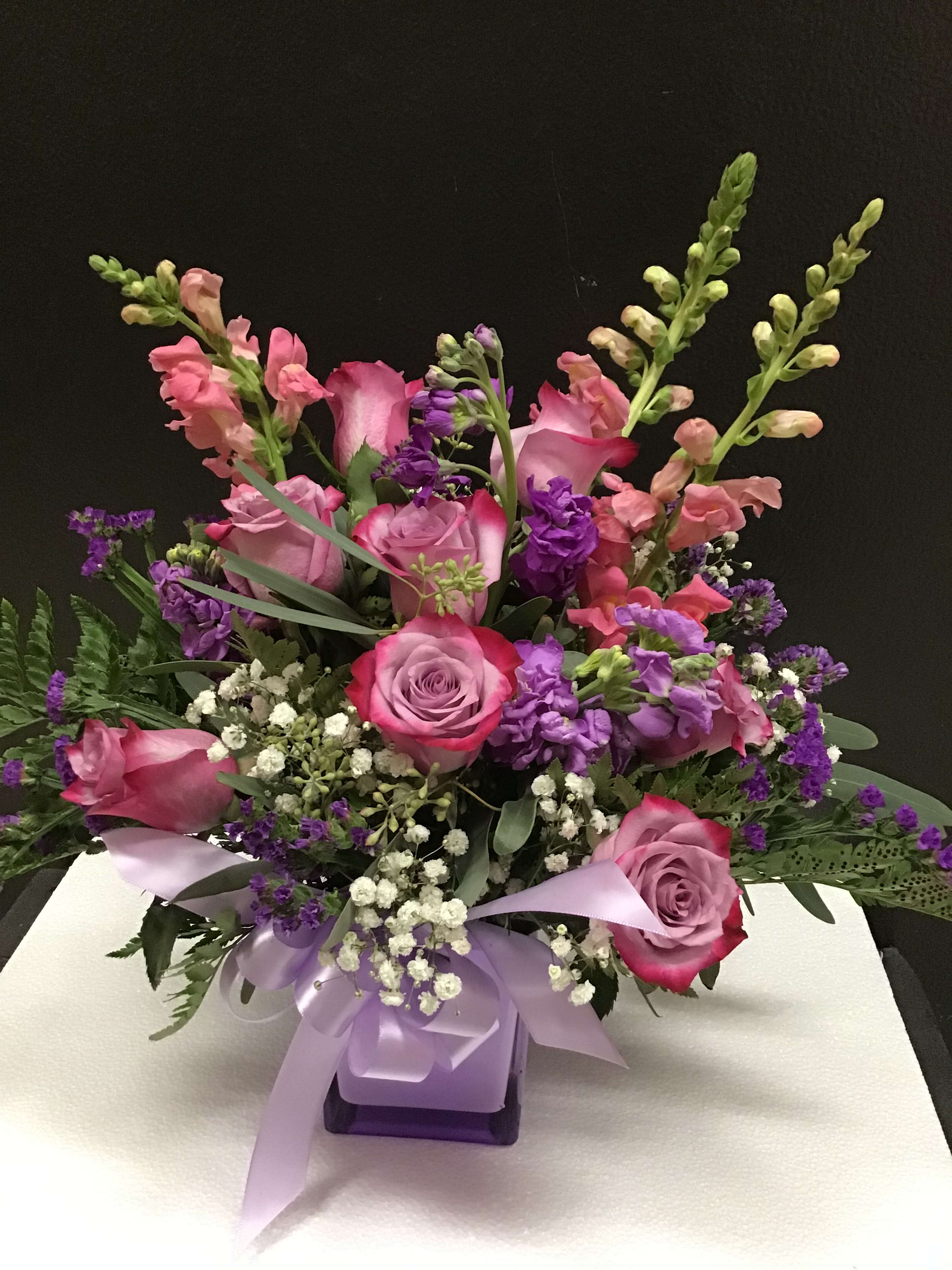 Pink and purple floral arrangement with roses and snapdragons in a ribbon-tied vase