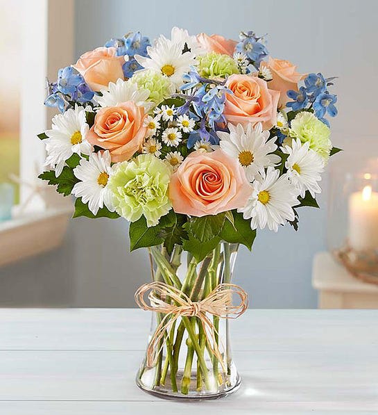 Bouquet of peach roses, white daisies, and blue flowers in a glass vase