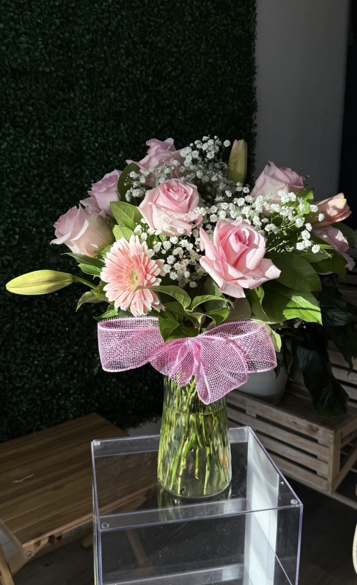 Pink roses and a gerbera daisy in a glass vase with a pink bow