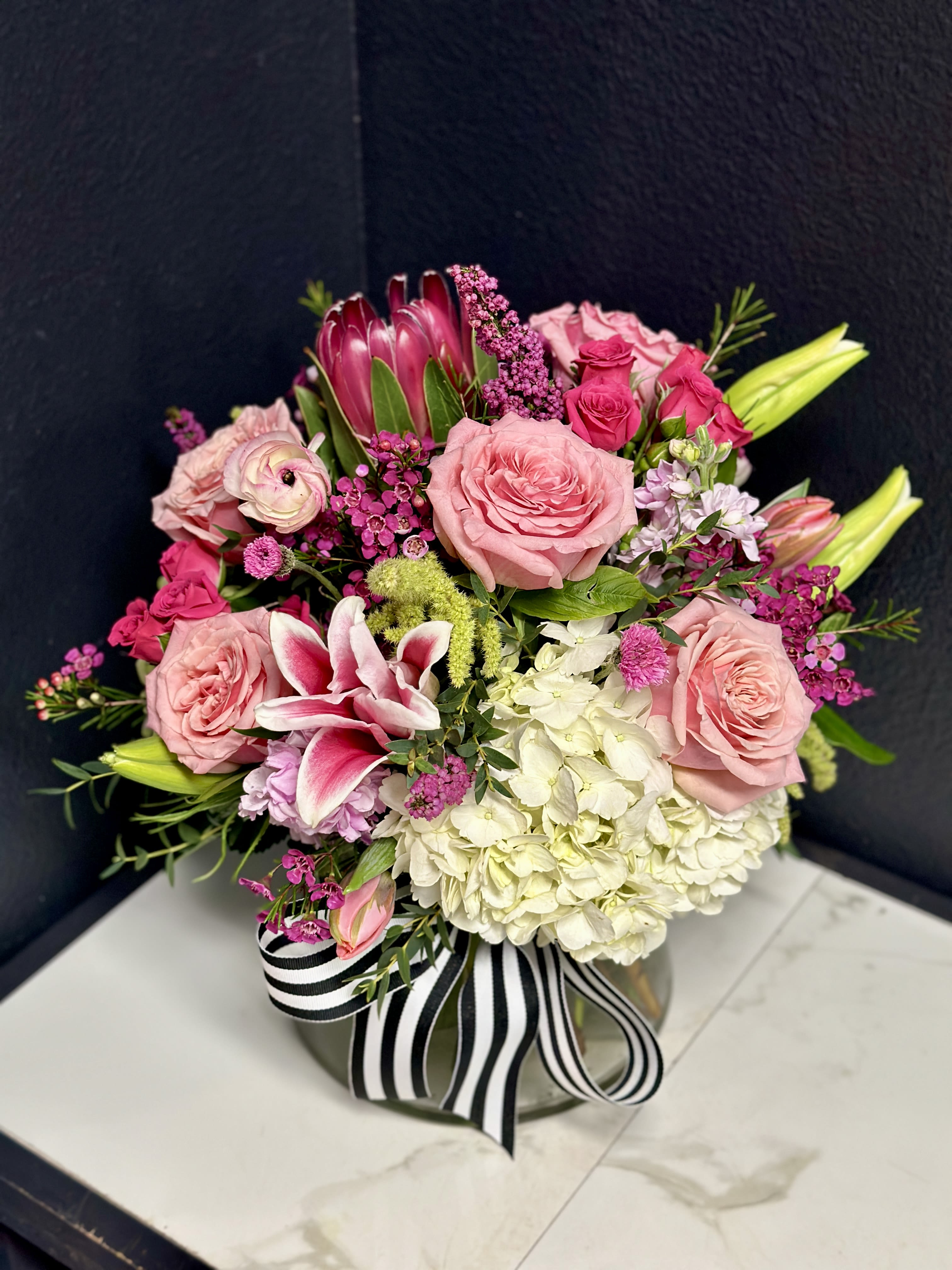 Pink and white floral arrangement in a round vase with a striped ribbon