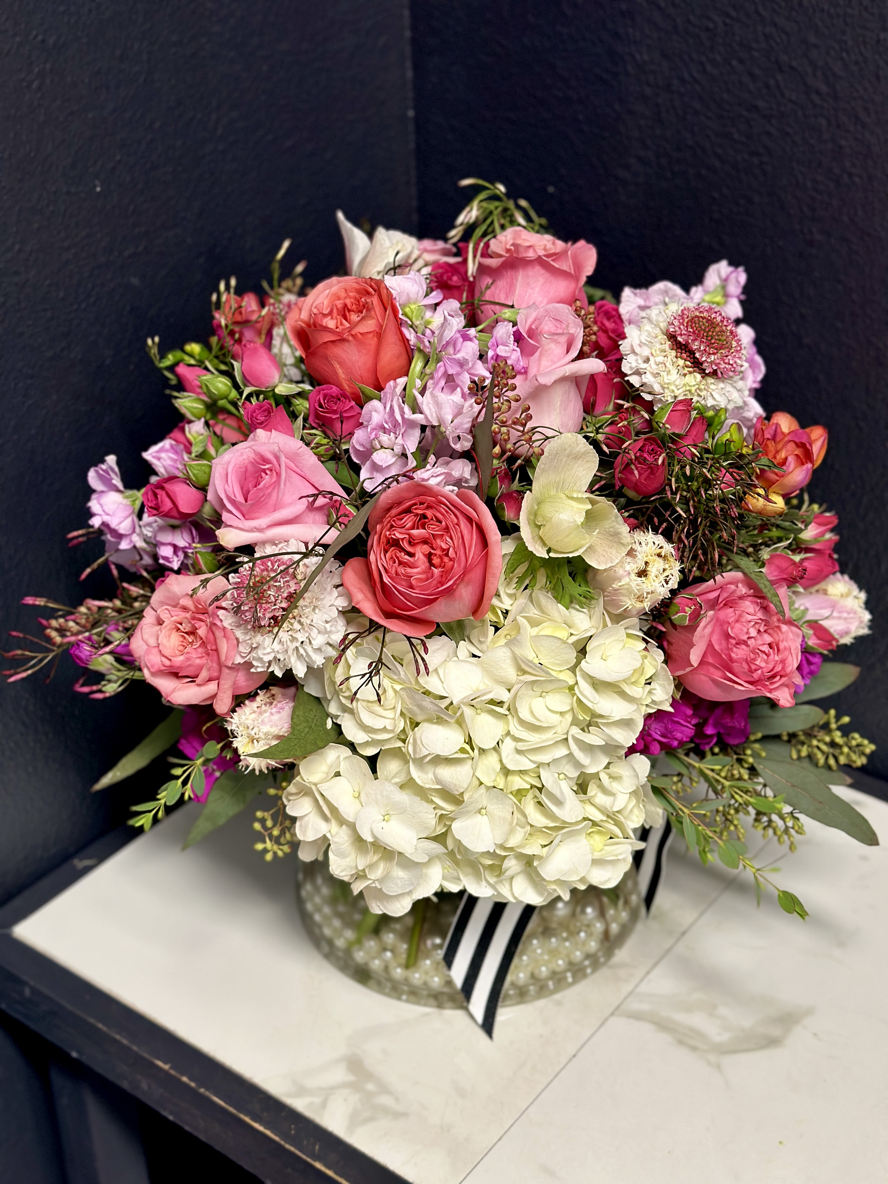 Pink and white rose bouquet in a clear glass vase with a striped ribbon