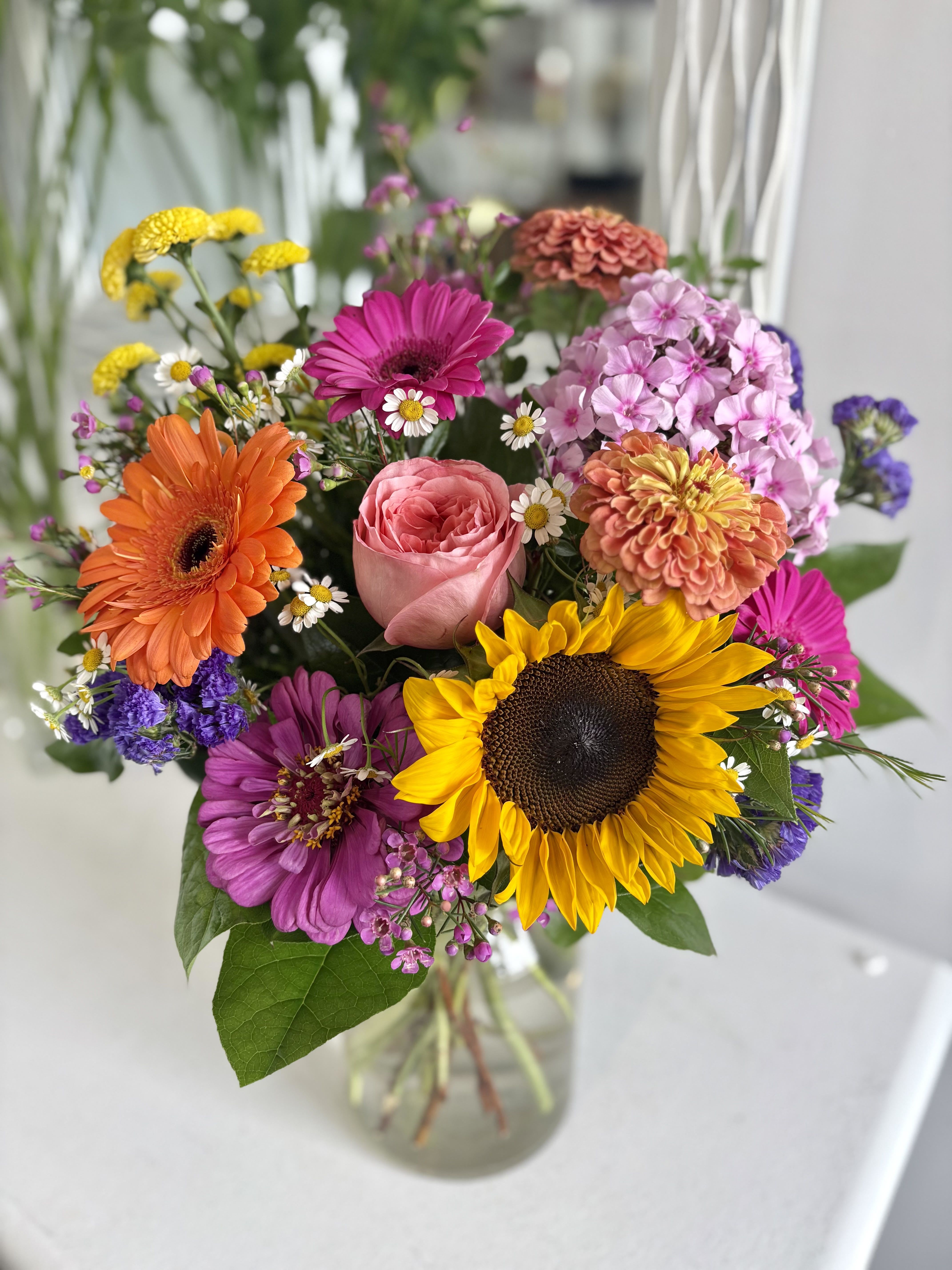 Bright mixed bouquet with sunflower, gerbera daisies, and a rose in a clear glass vase
