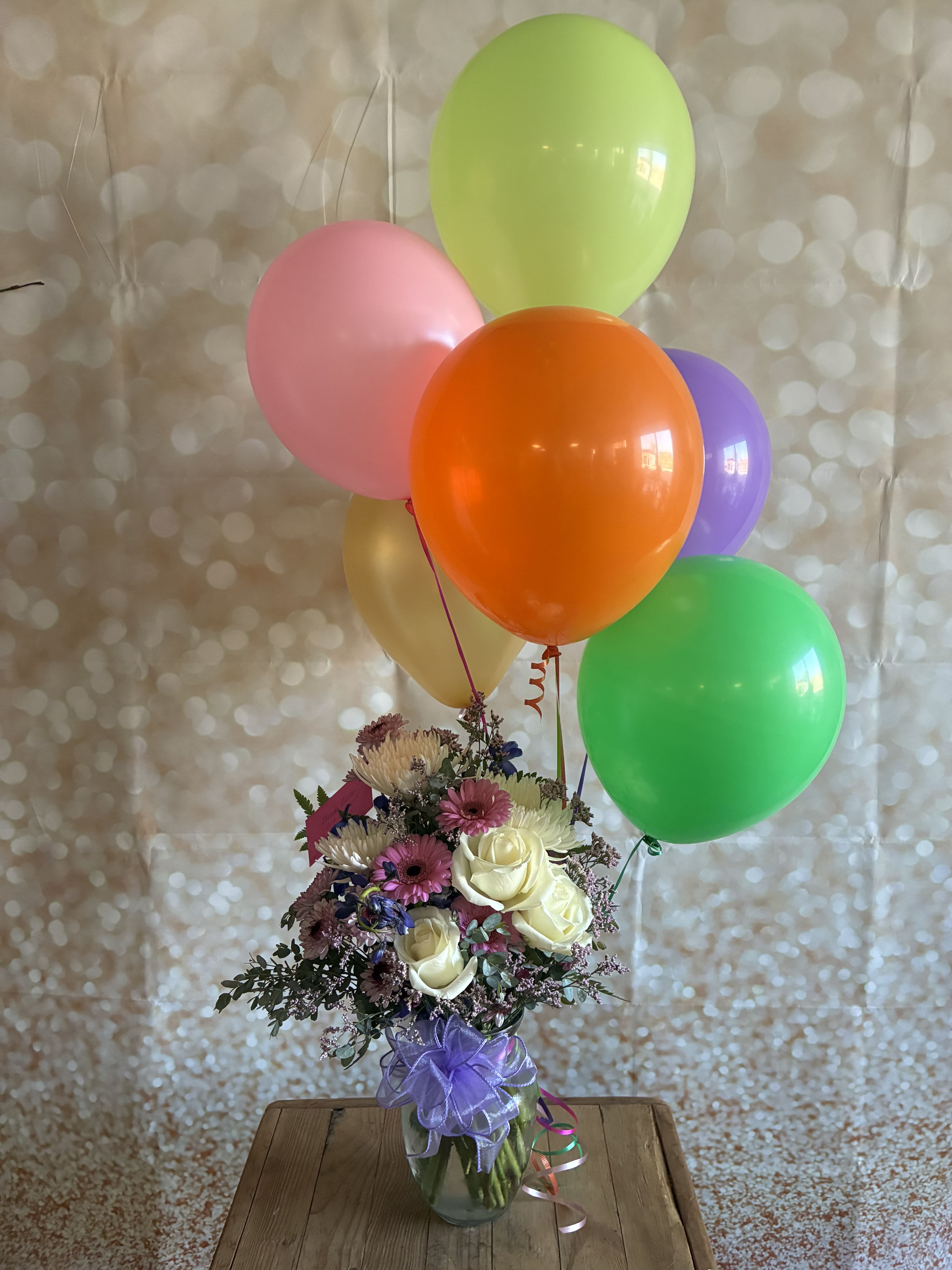 Bouquet of mixed flowers in a glass vase with colorful balloons