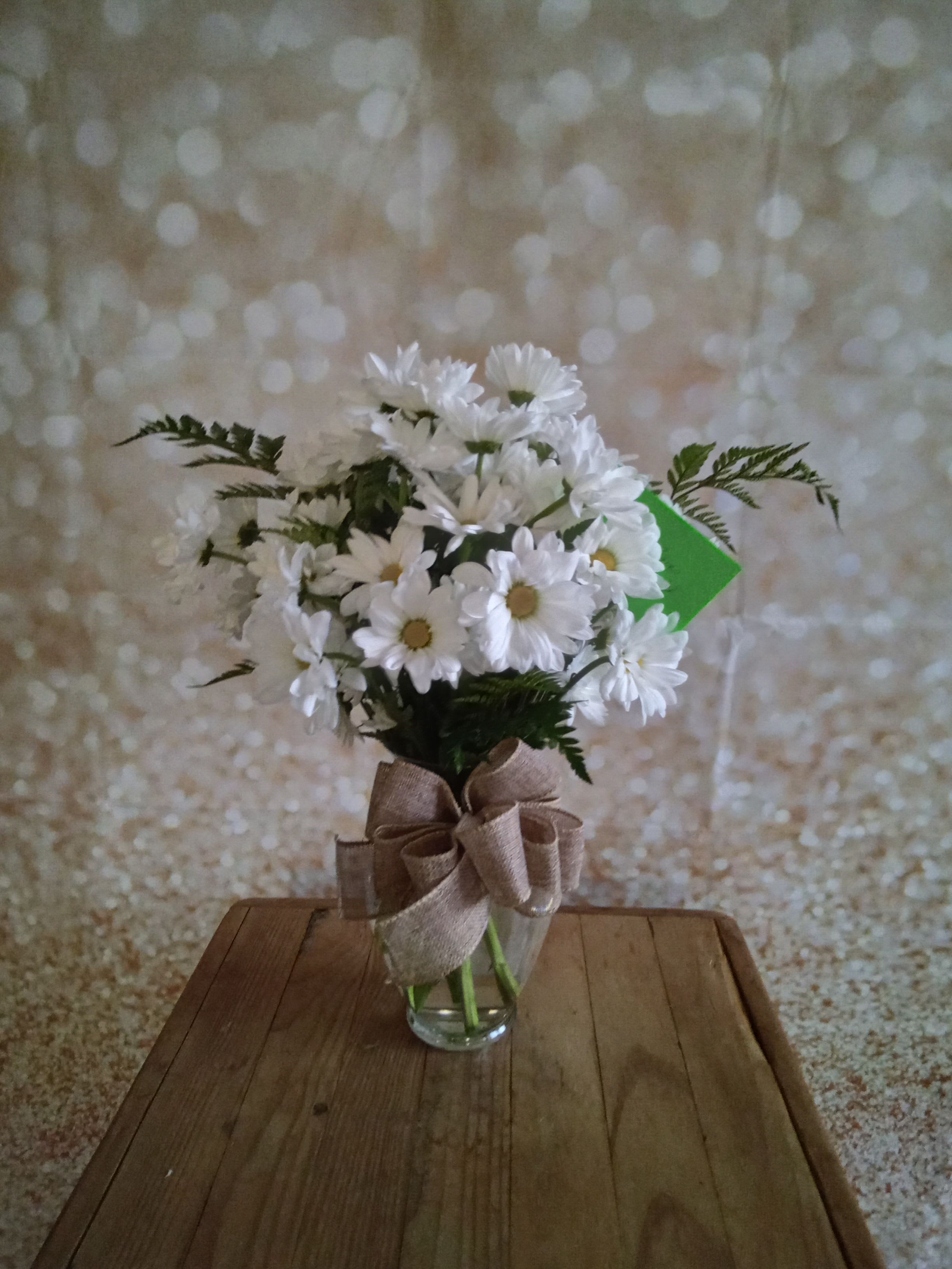 White daisy bouquet in a clear glass vase with a burlap bow
