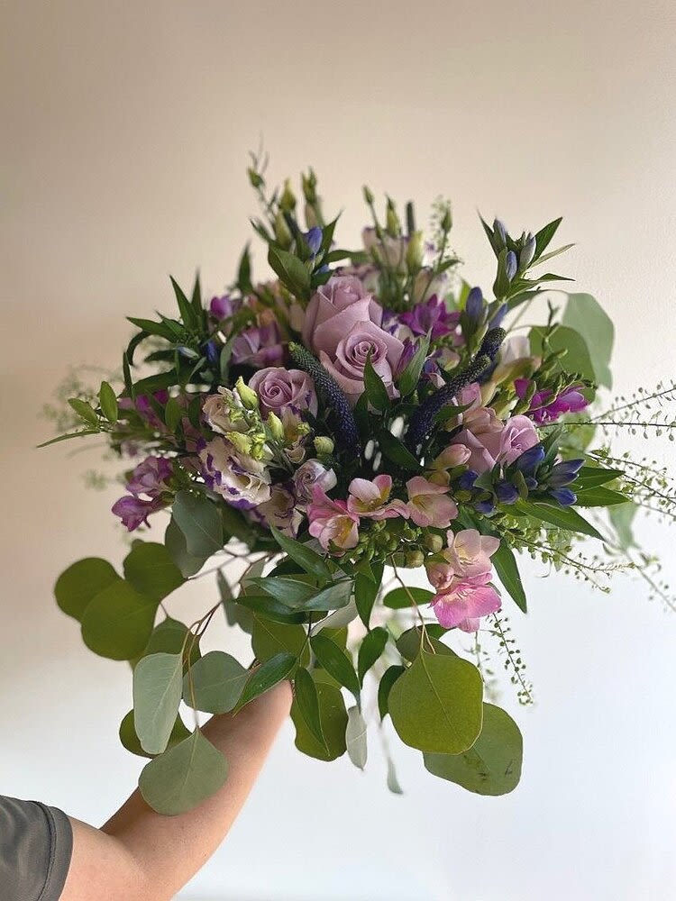 Handheld bouquet of lavender roses and purple flowers with trailing greenery