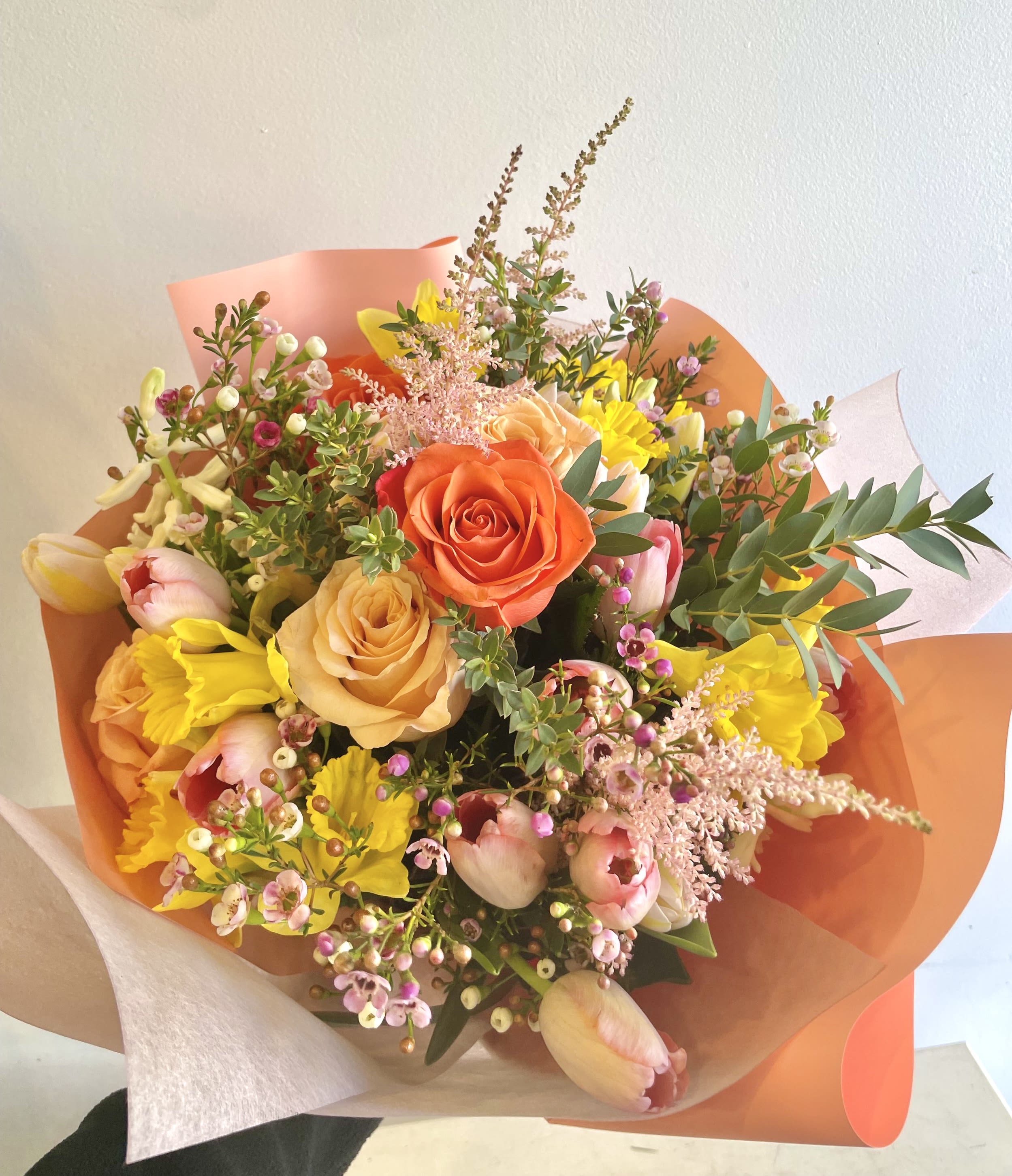 Bouquet of orange, peach, pink, and yellow flowers wrapped in coral paper