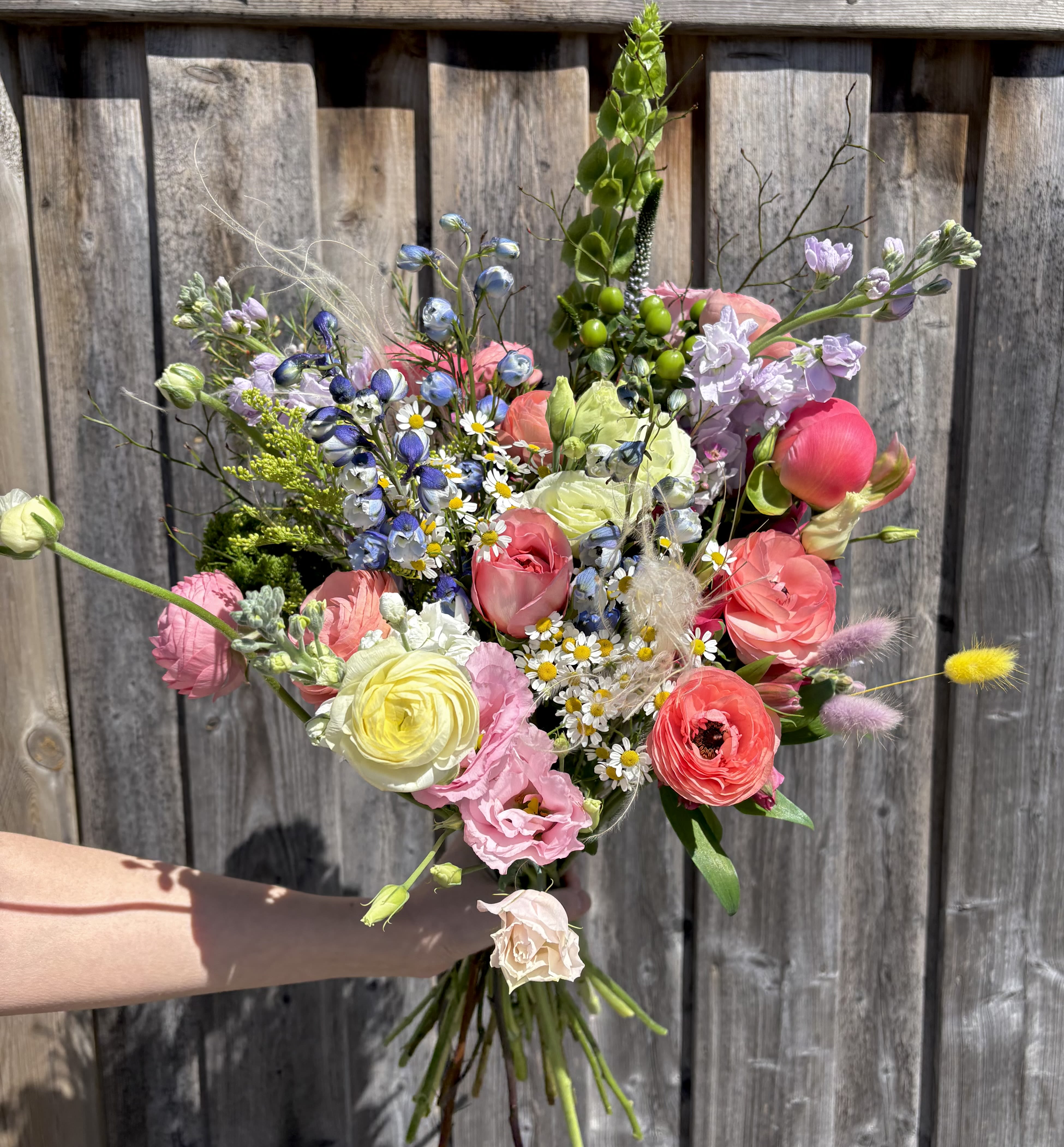 Handheld bouquet of mixed pastel flowers with tall greenery