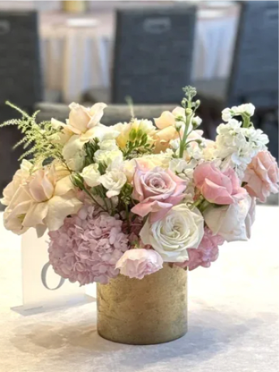 Pastel arrangement of pink hydrangeas and blush and ivory roses in a gold cylinder vase