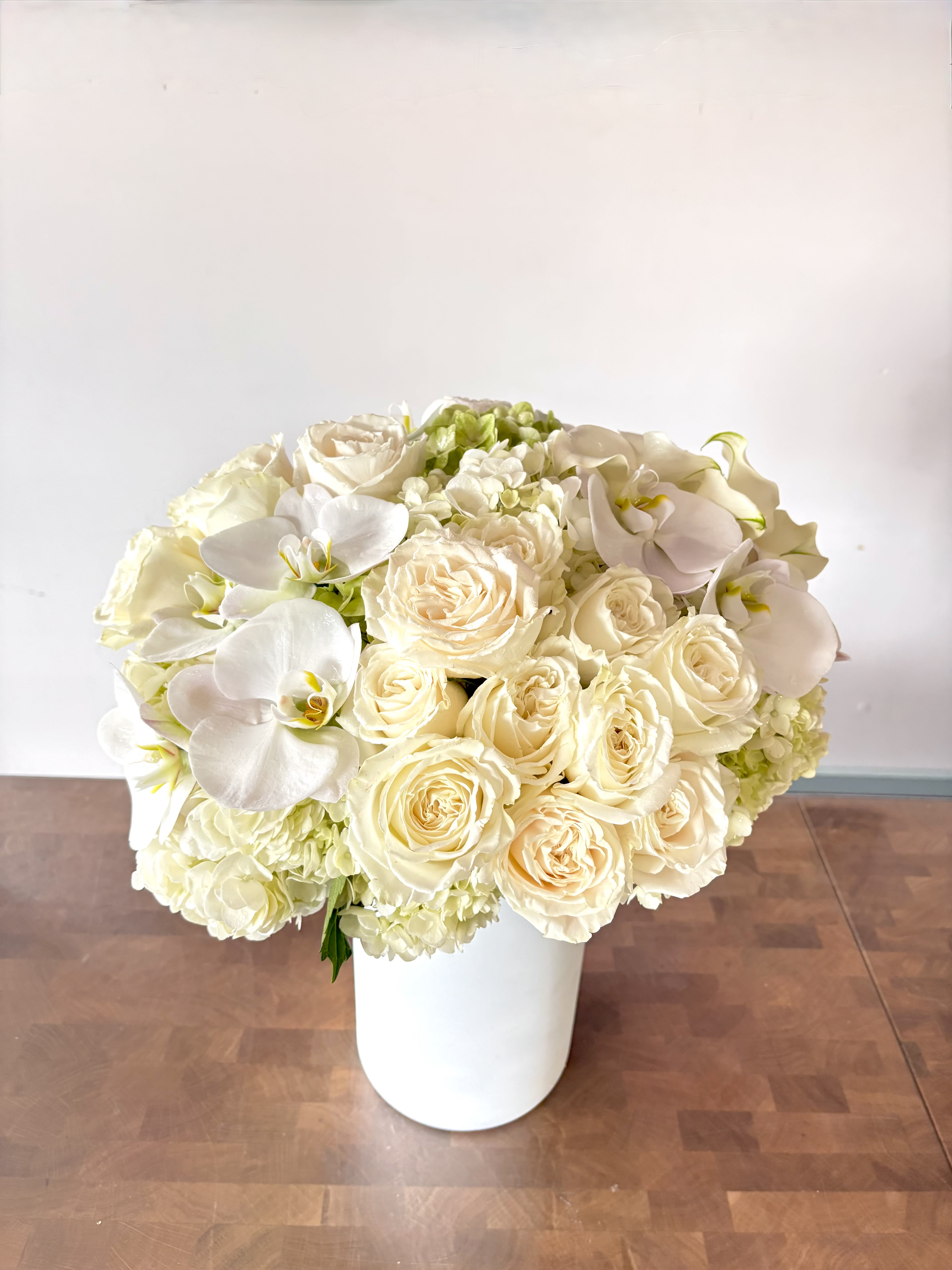 Cream roses and white orchids arranged in a white vase