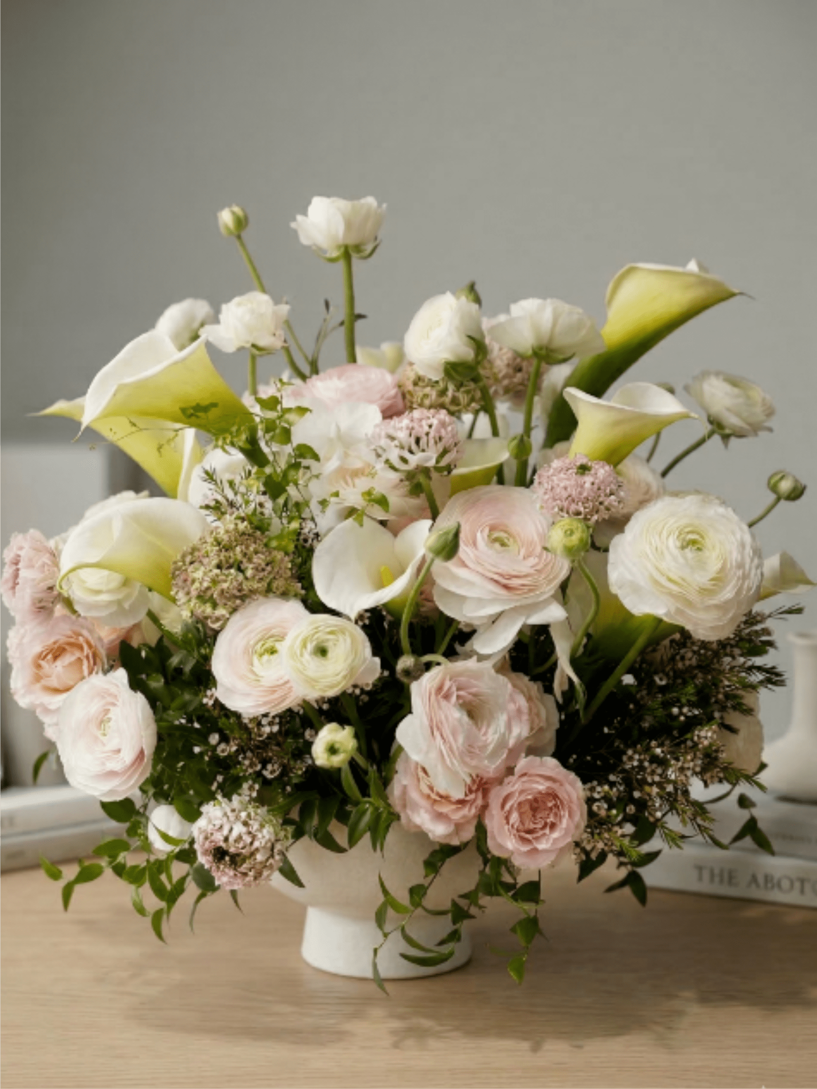 Low arrangement of white calla lilies and pale pink blooms in a white footed bowl
