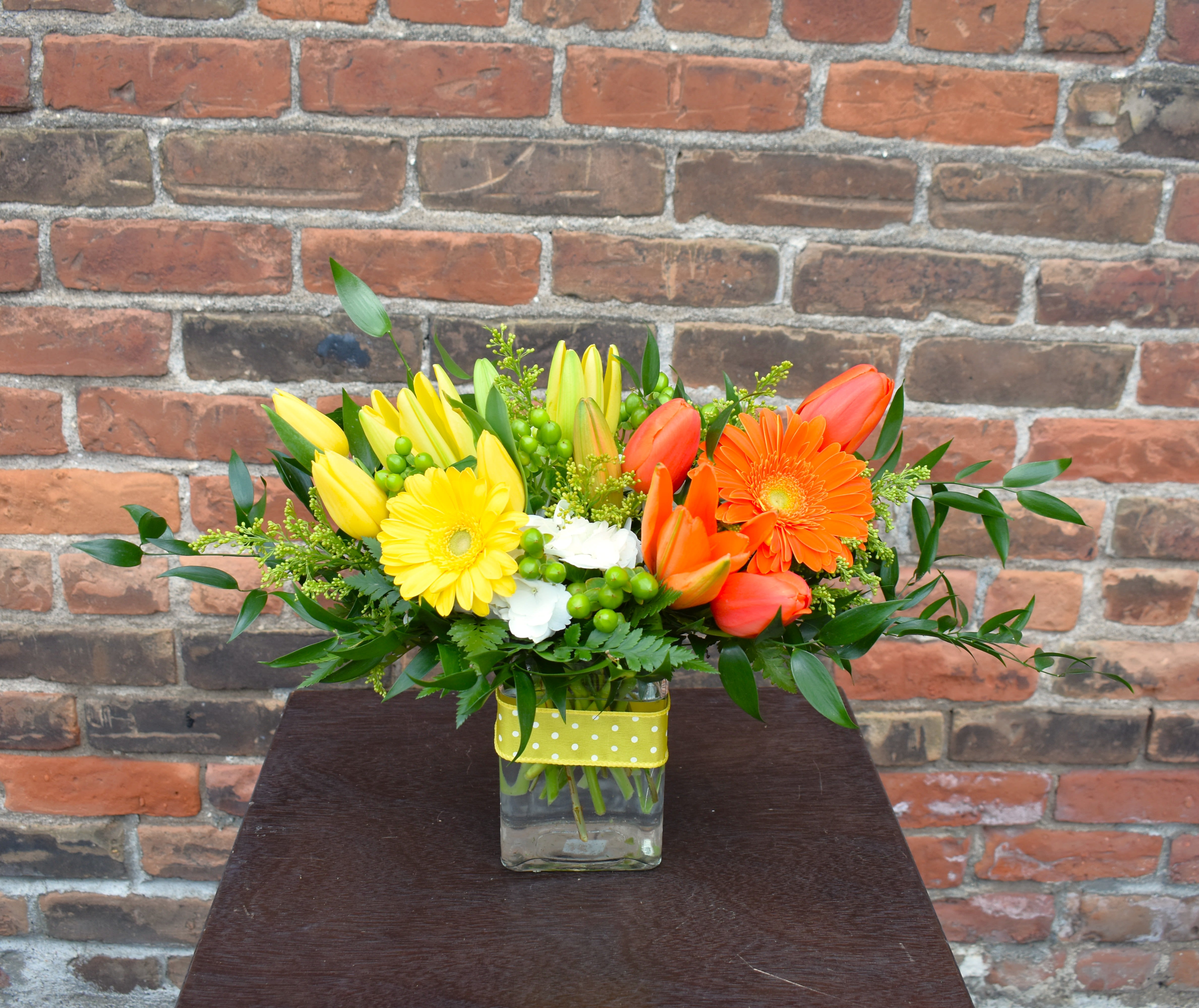 Mimosa - Cheers to Mom! Yellow &amp; orange lilies, tulips, and Gerber daisies accompany hydrangea, asters, hypericum and lush greens; all designed in a vase and accented with yellow ribbon...the perfect treat for Mom!  