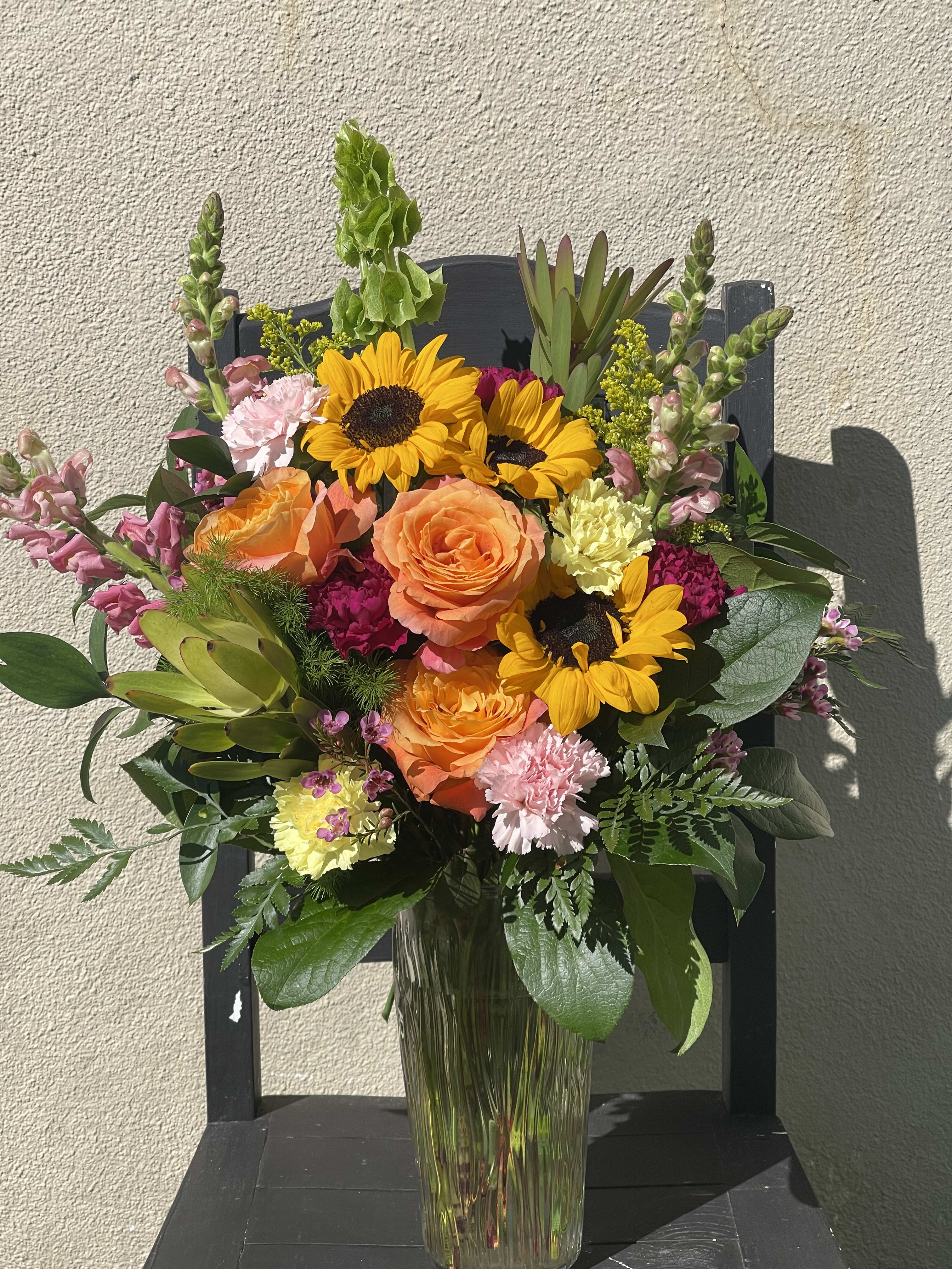Tall mixed bouquet with sunflowers, orange roses, and pink flowers in a clear glass vase