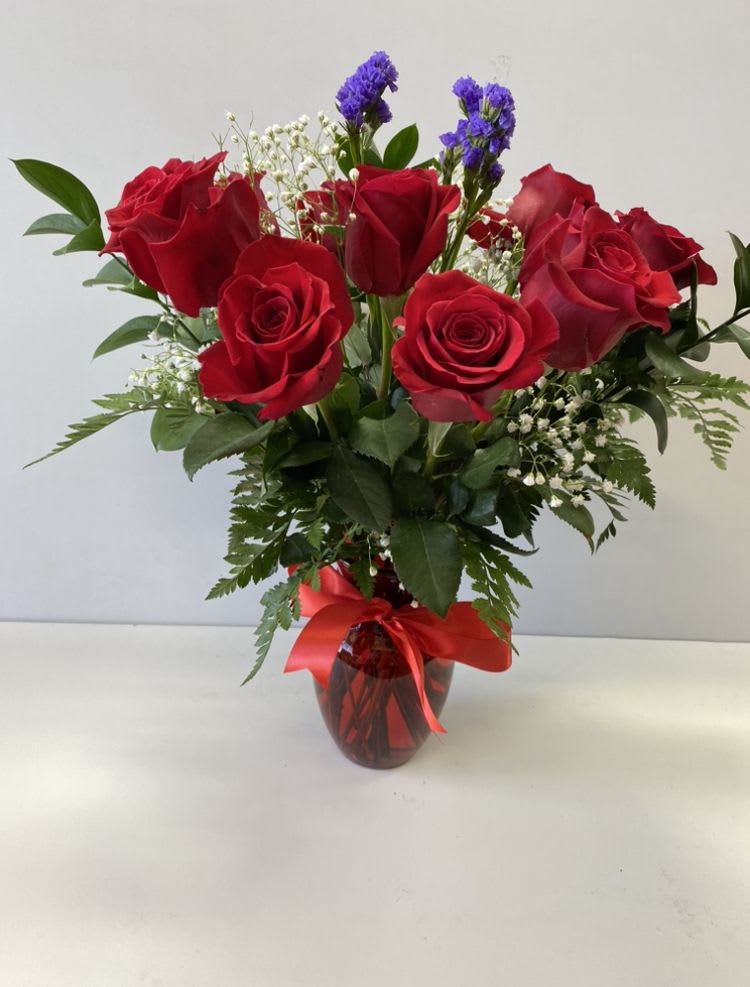 Red roses with white and purple filler flowers in a red vase with a red ribbon bow
