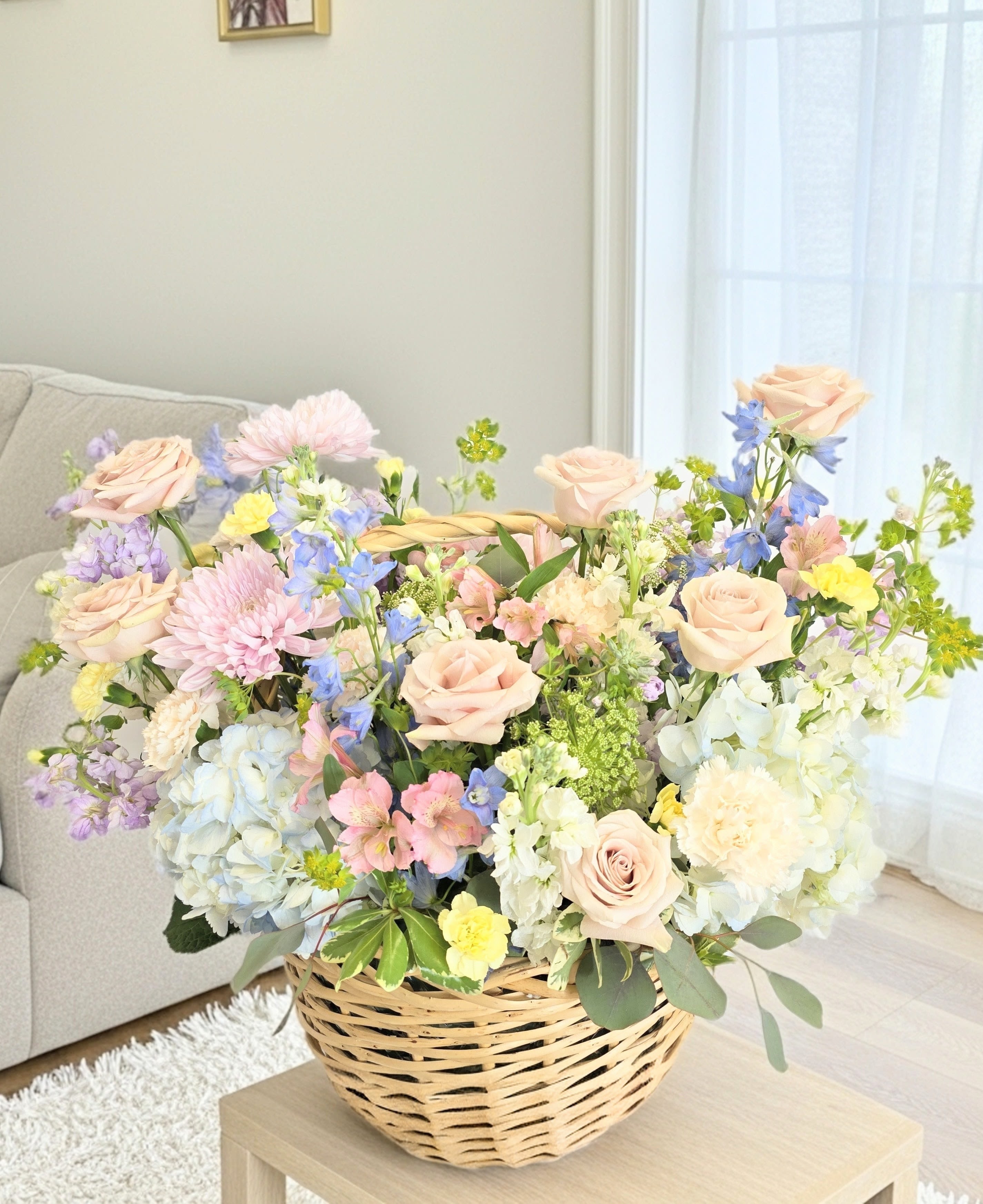 Mom's Delightful Garden  - A generous, garden-style basket that feels like a sunlit spring morning - Mom's Delightful Garden is a large flower arrangement perfect as a birthday bouquet, Mother's Day gift, or a cheerful thank-you gesture. Soft blush roses and pale blue hydrangeas take center stage, while pink and yellow accents and airy blue delphinium spikes give the composition a layered, romantic look that will make the person you're thinking of feel loved. 