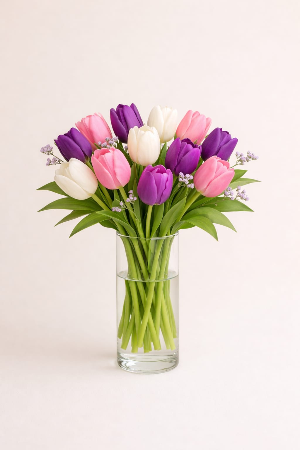 Spring Harmony Tulip Vase - A cheerful mix of three or more tulip colors, loosely gathered with soft touches of filler flowers in a clear cylindrical glass vase. Bright, fresh, and effortlessly elegant — a perfect nod to spring’s natural beauty.