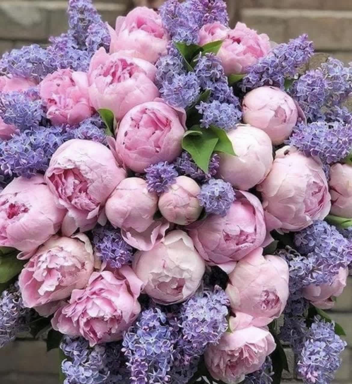 Pink peonies mixed with purple lilac blooms in a dense bouquet