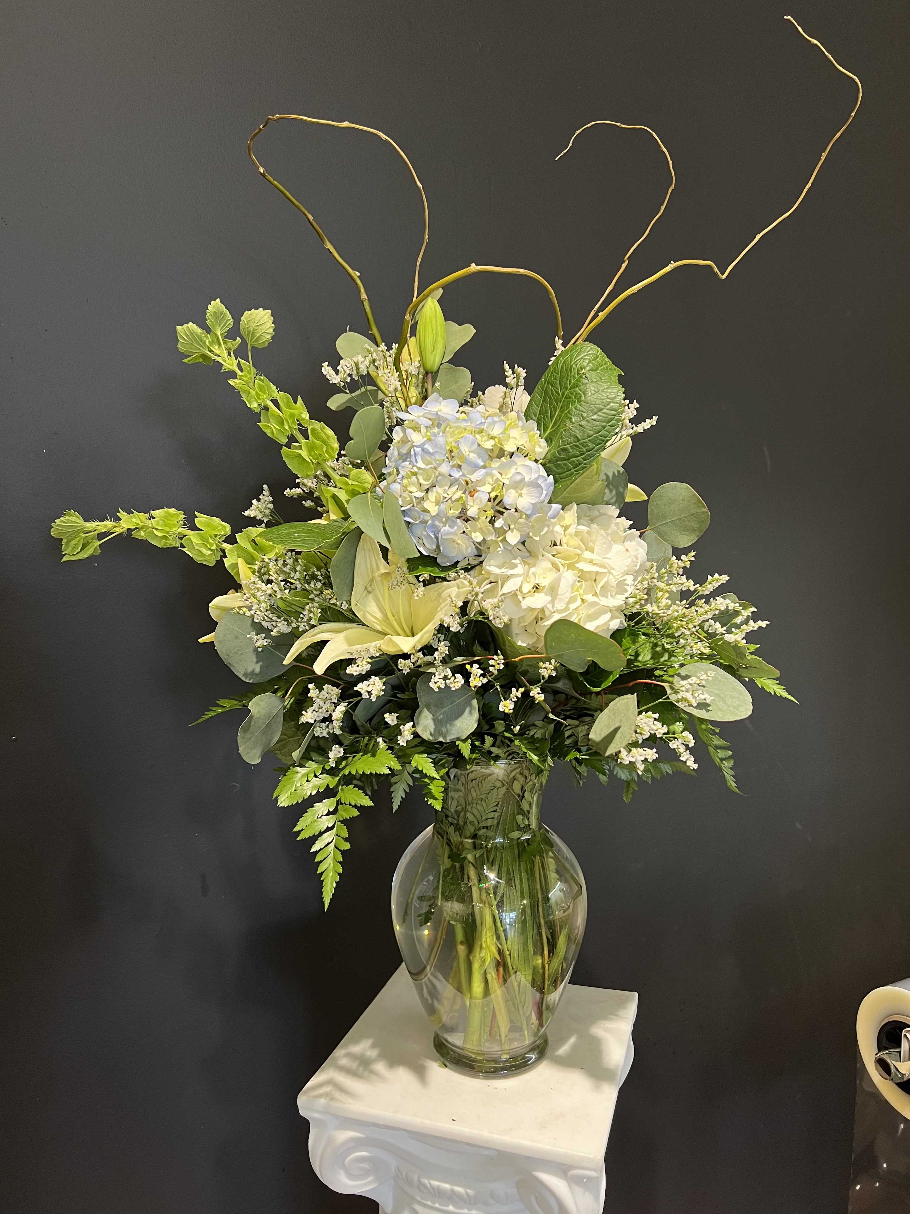 Tall white and pale blue floral arrangement in a glass vase