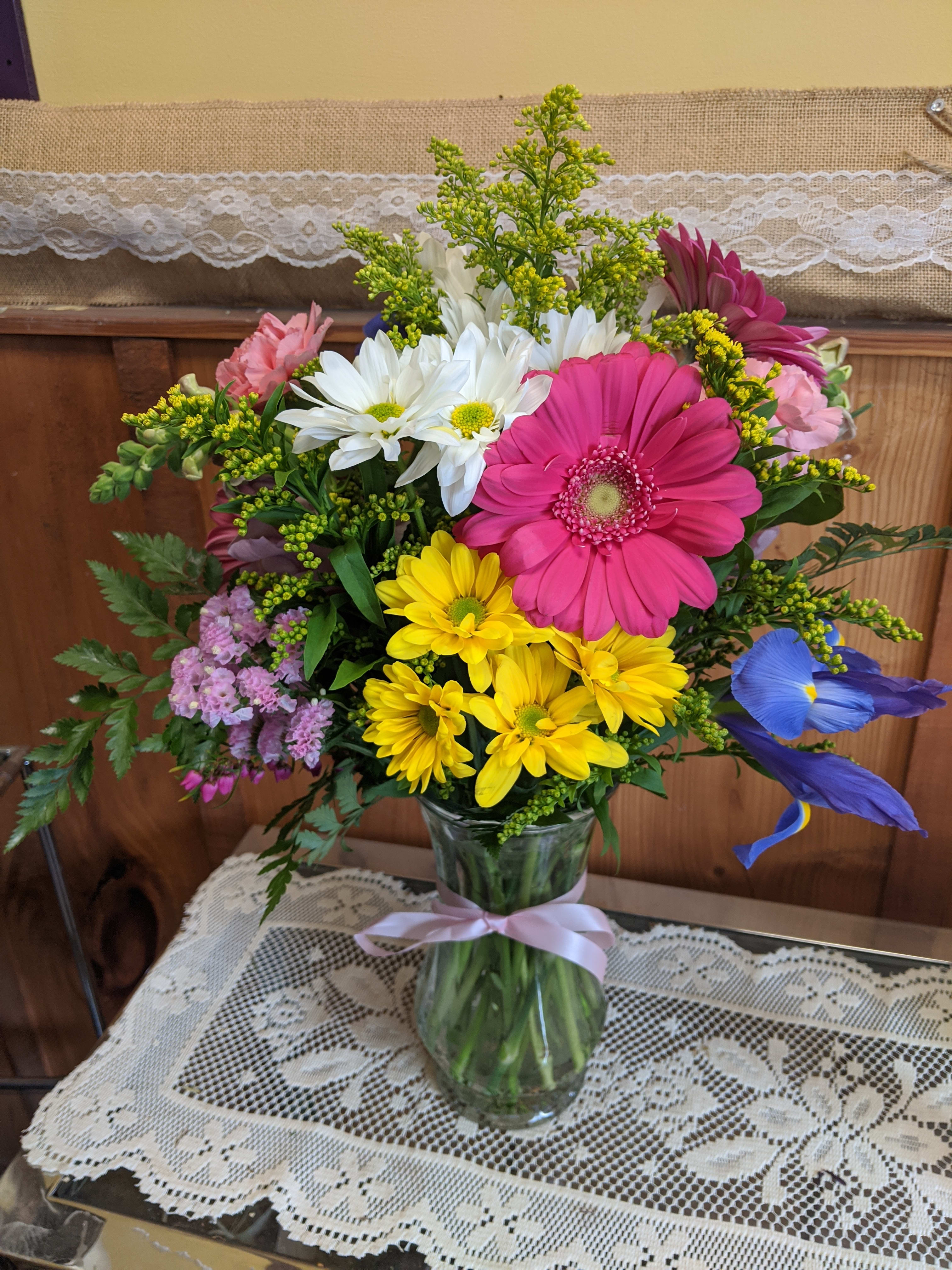 Mixed bouquet in a glass vase with pink, yellow, white, and blue flowers
