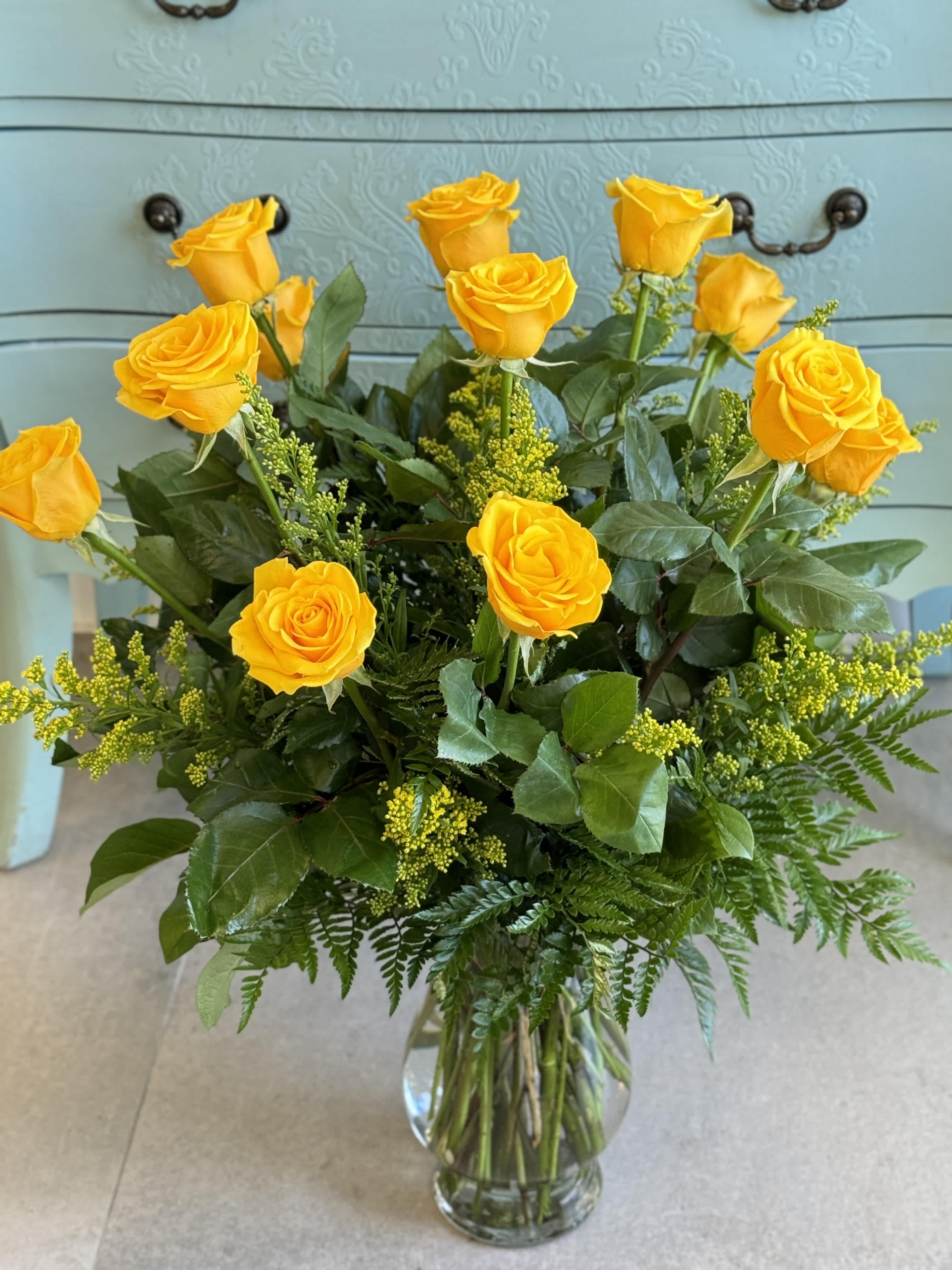 Yellow roses arranged in a clear glass vase with greenery