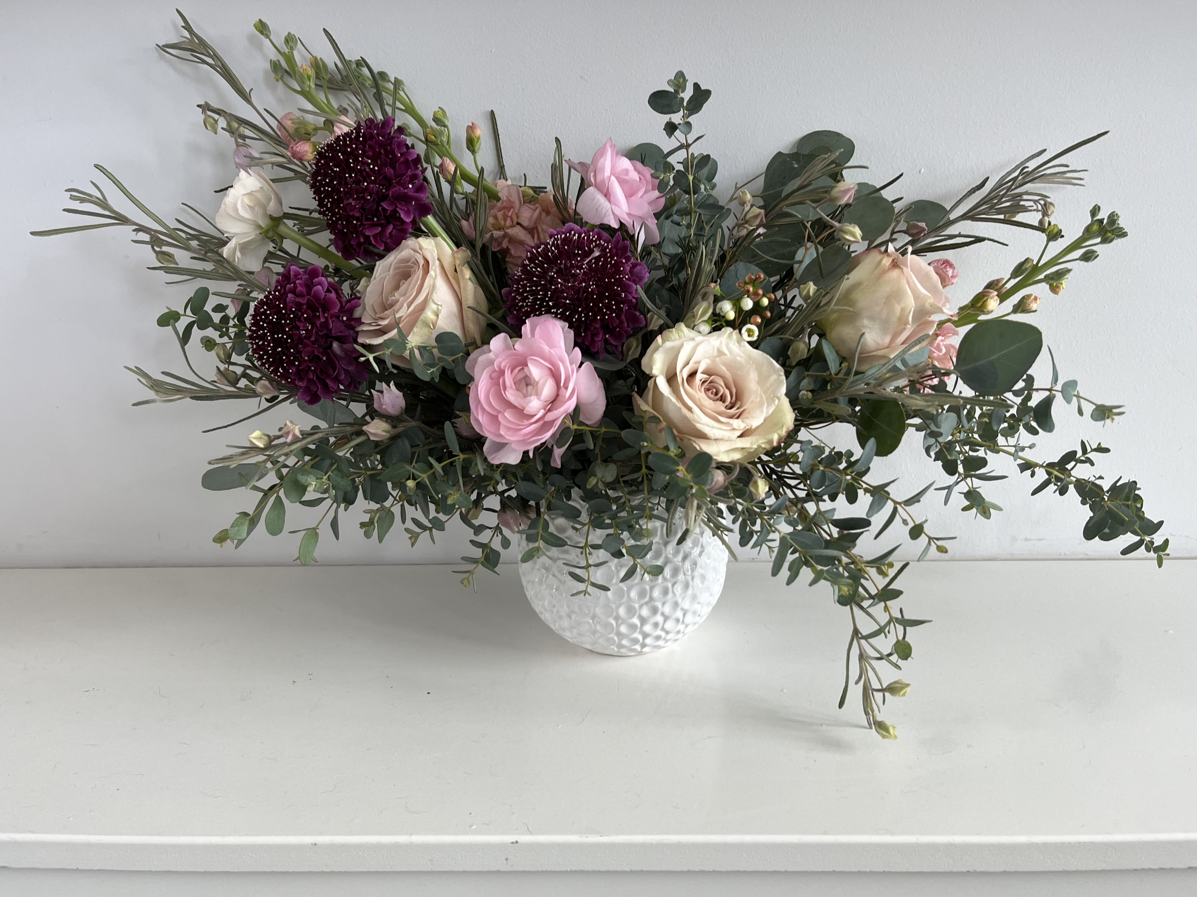 Pink and cream roses with dark purple blooms in a white vase
