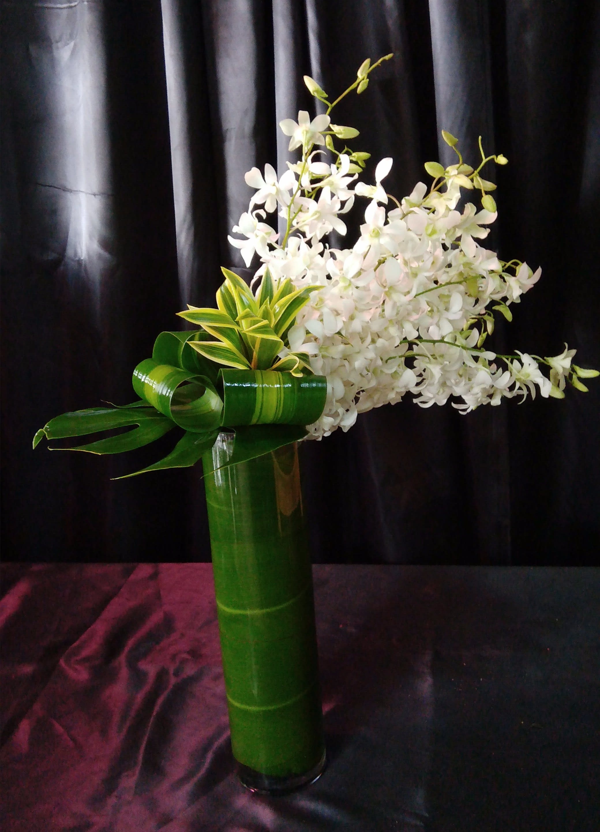 White orchid arrangement in a tall green vase with curled leaves