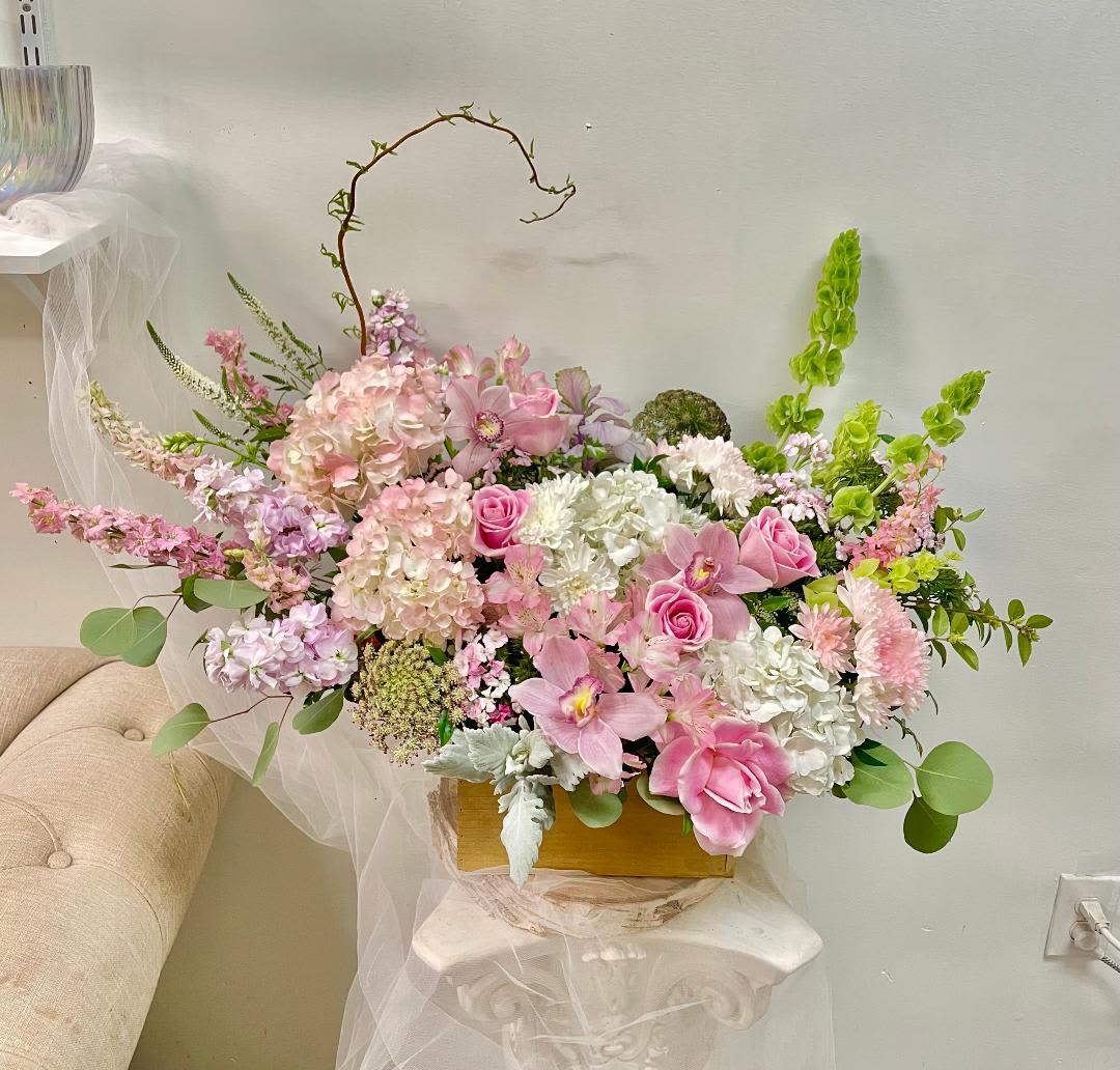 Pink and white floral arrangement in a gold box with arching branches