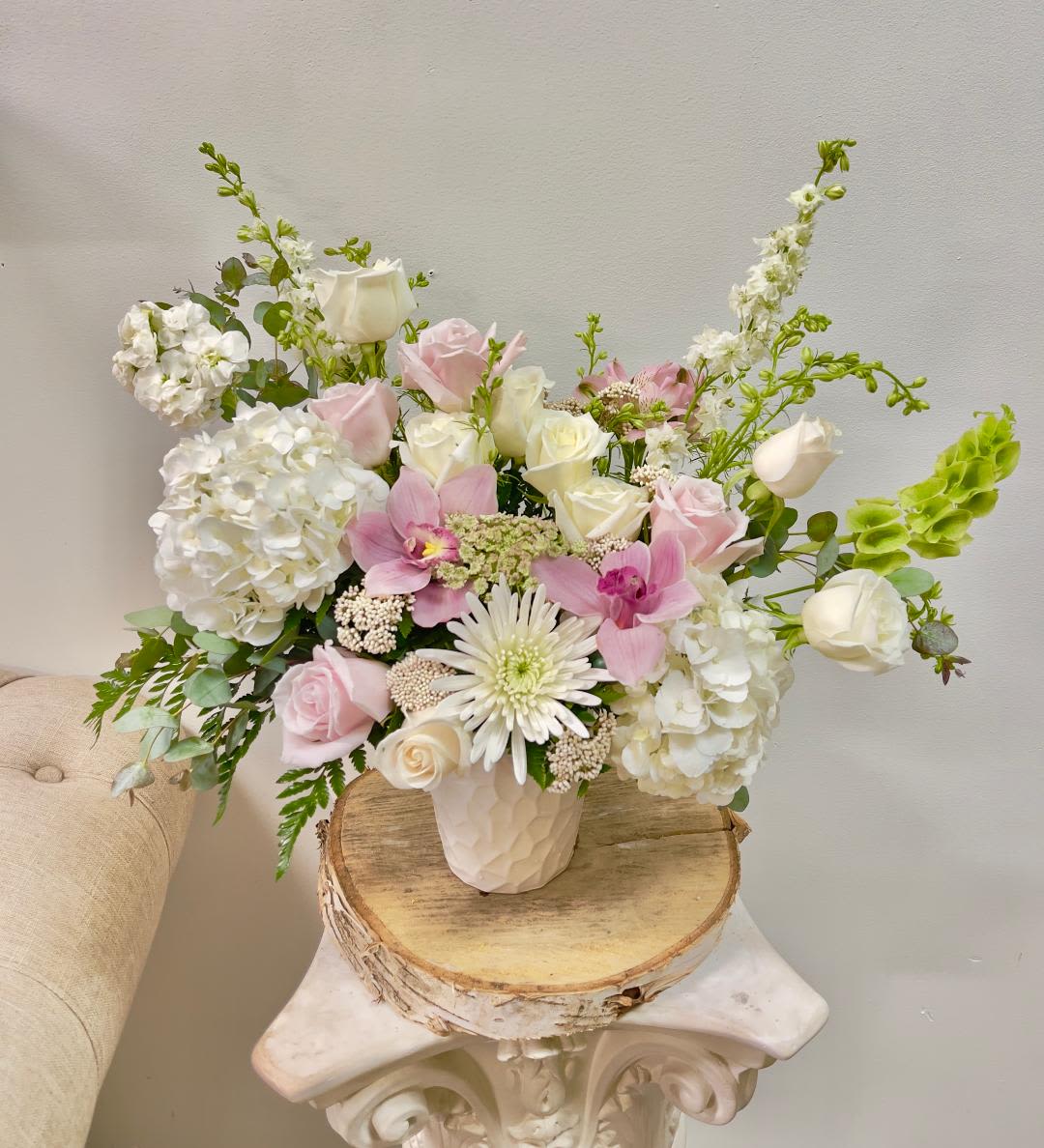 Pink and white roses with orchids and hydrangeas in a white vase