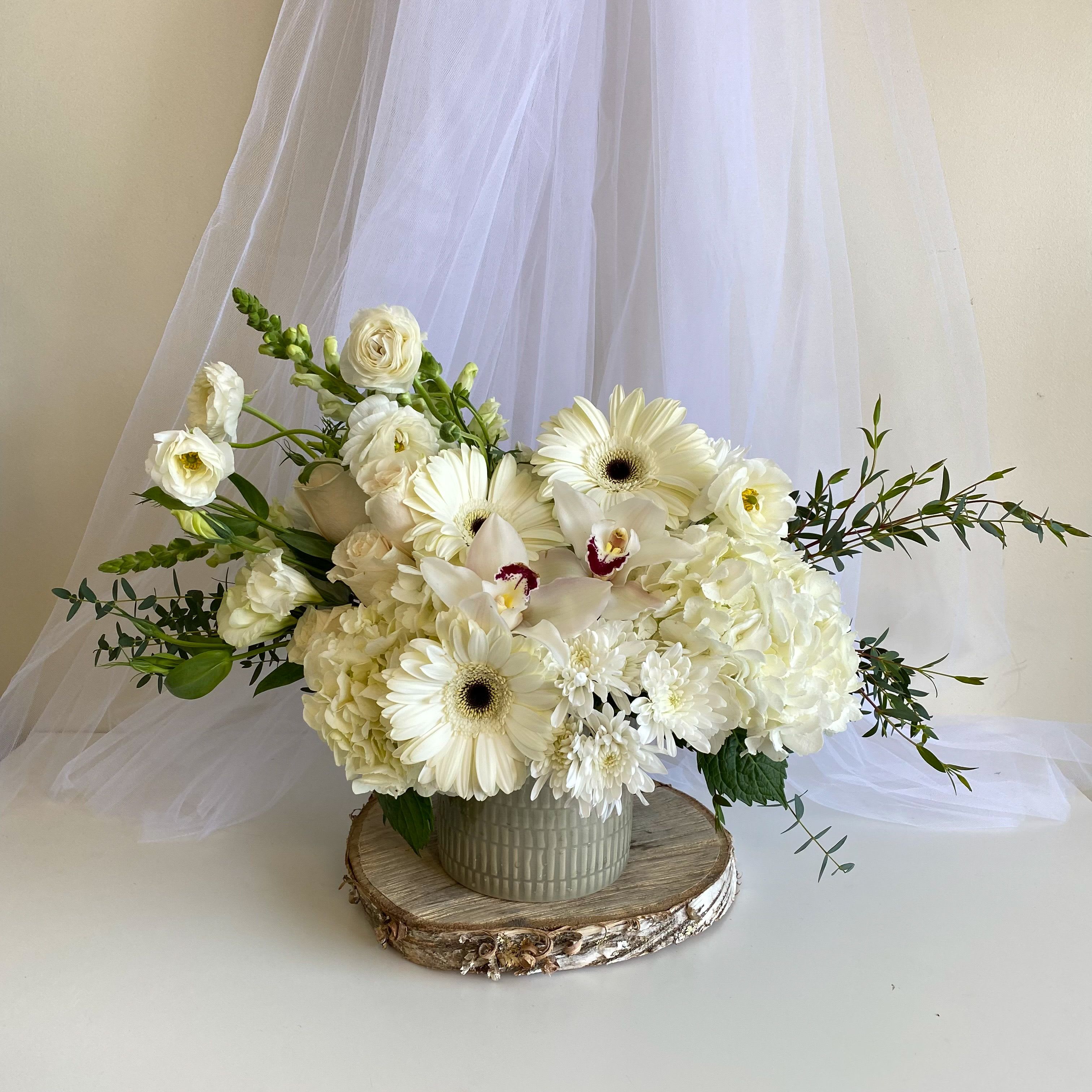 White floral arrangement in a ceramic vase with trailing greenery