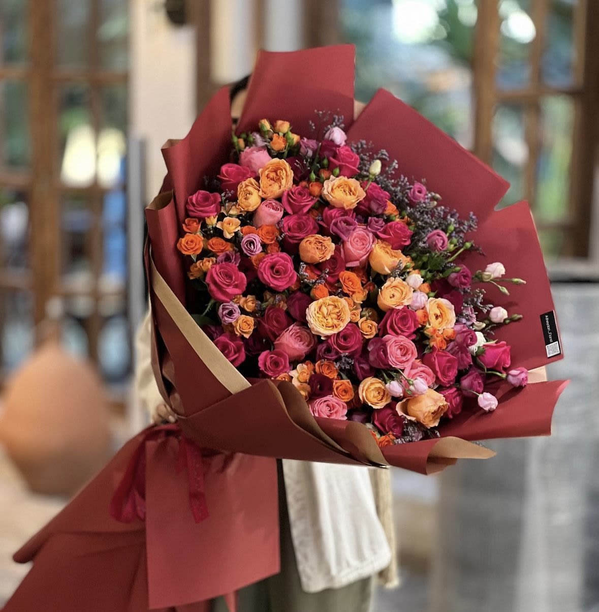 Large bouquet of pink and orange roses wrapped in burgundy paper