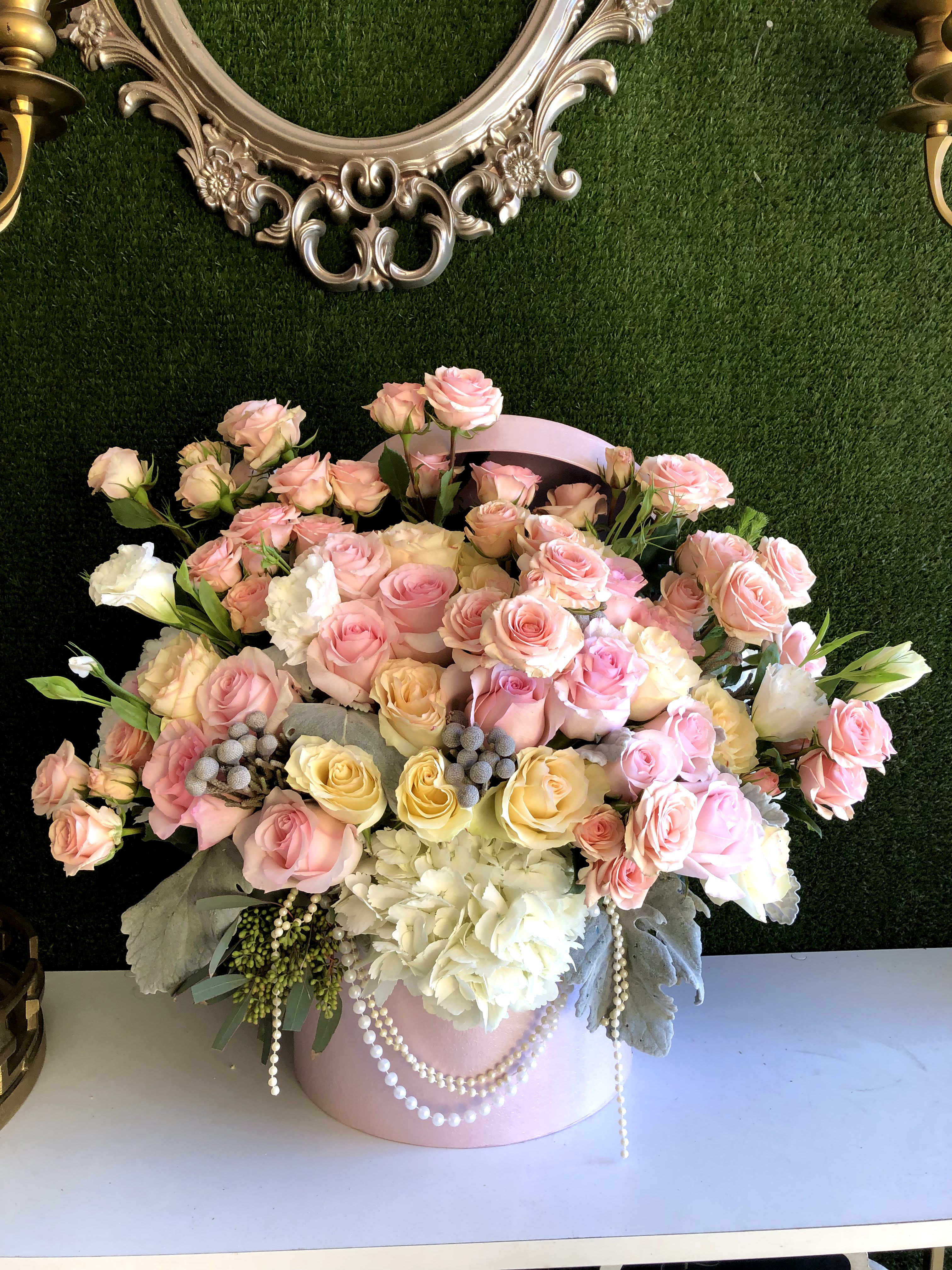 Large arrangement of pink and yellow roses with white hydrangeas in a pink hatbox with pearl accents