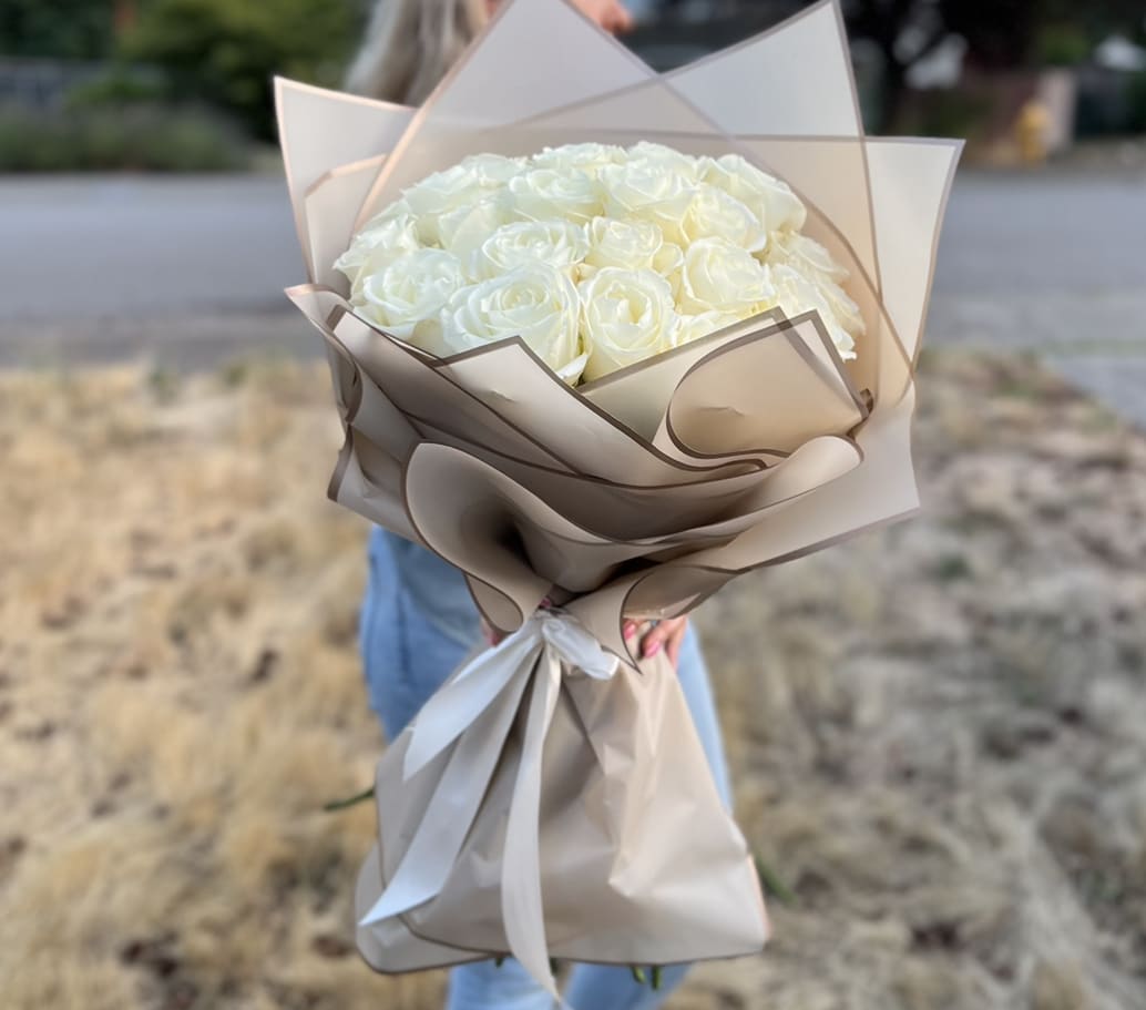 Bouquet of white roses wrapped in beige paper with a white ribbon