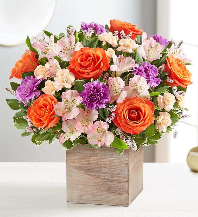 Mixed bouquet of orange roses, pink alstroemeria, and purple carnations in a wooden box