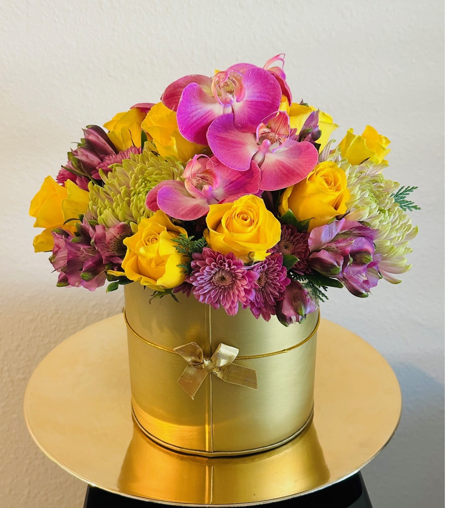 Pink orchids and yellow roses in a gold round box