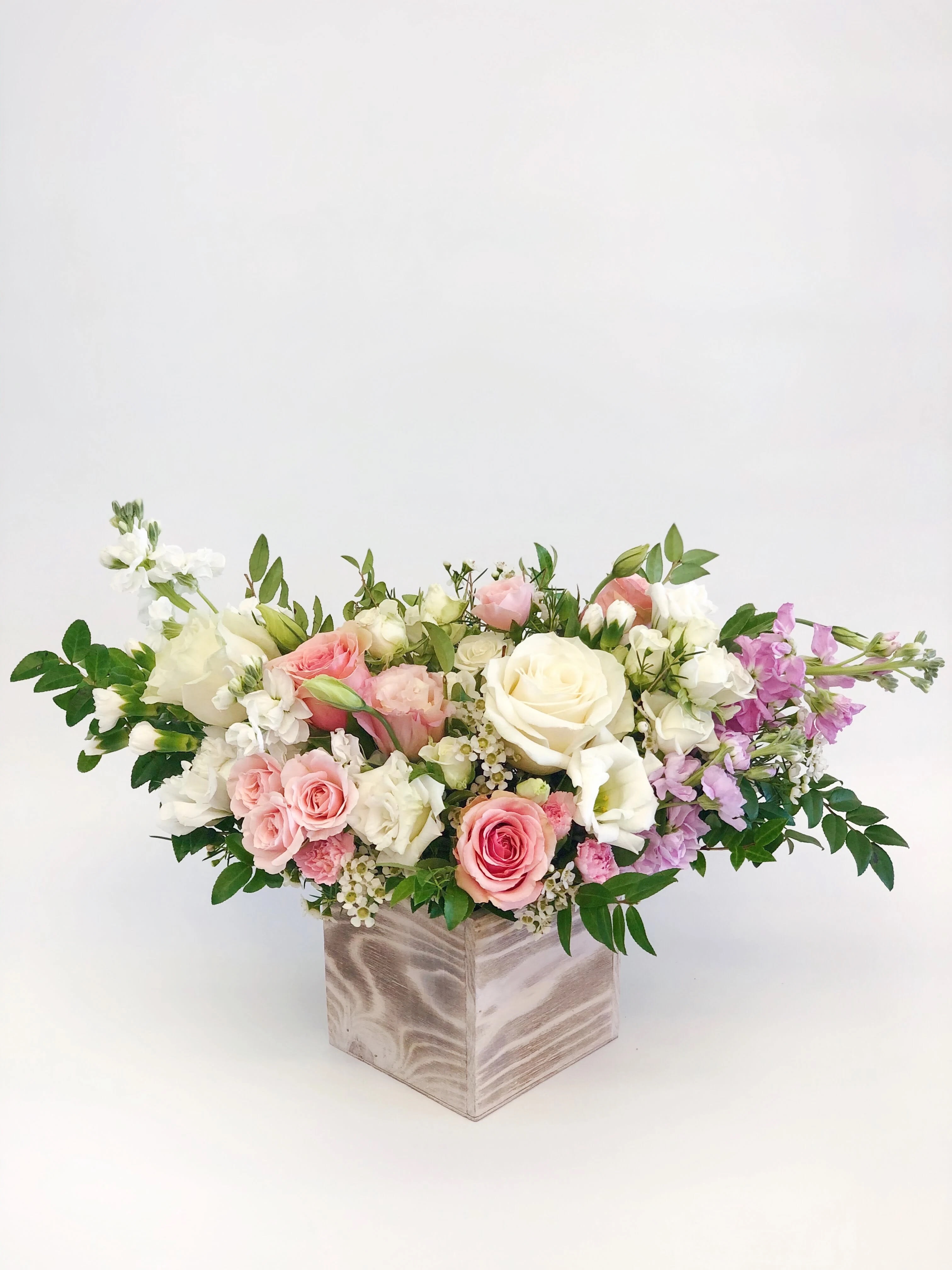 Low floral arrangement of pink, white, and lavender roses in a square vase