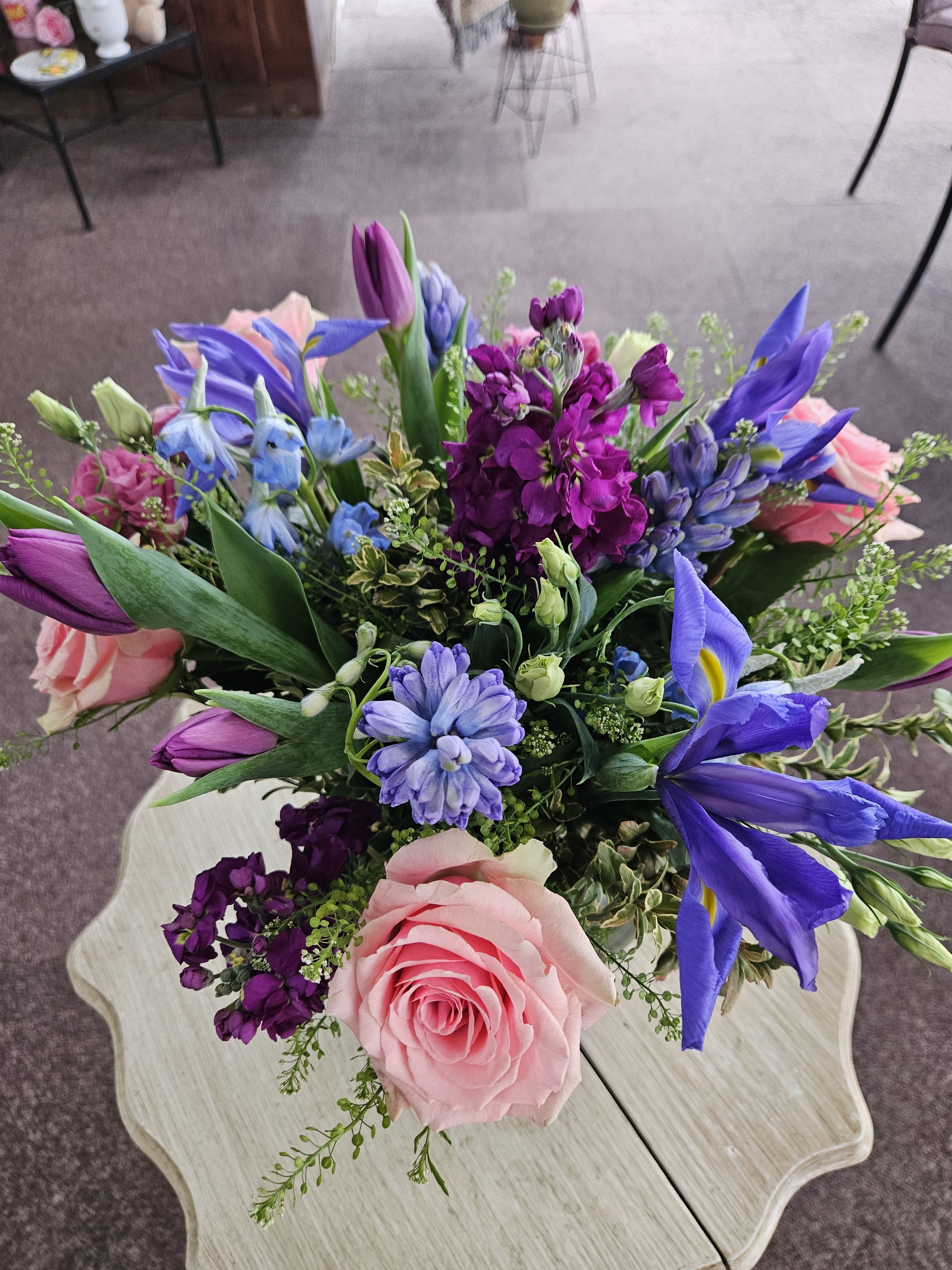 Colorful bouquet with pink roses, purple stock, tulips, blue iris and hyacinth on a light wood table
