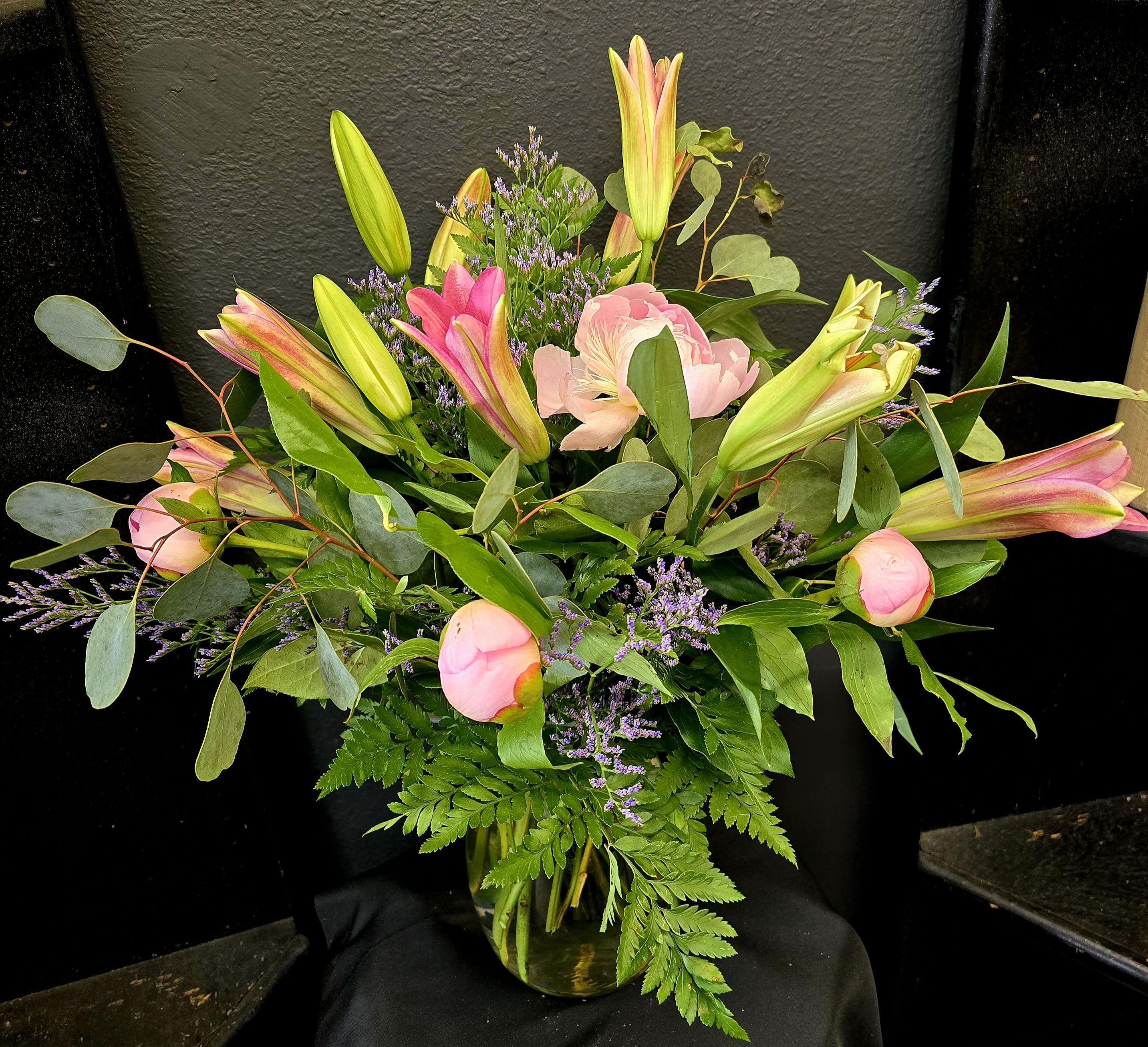 Pink lilies and peonies arranged in a glass vase with greenery.
