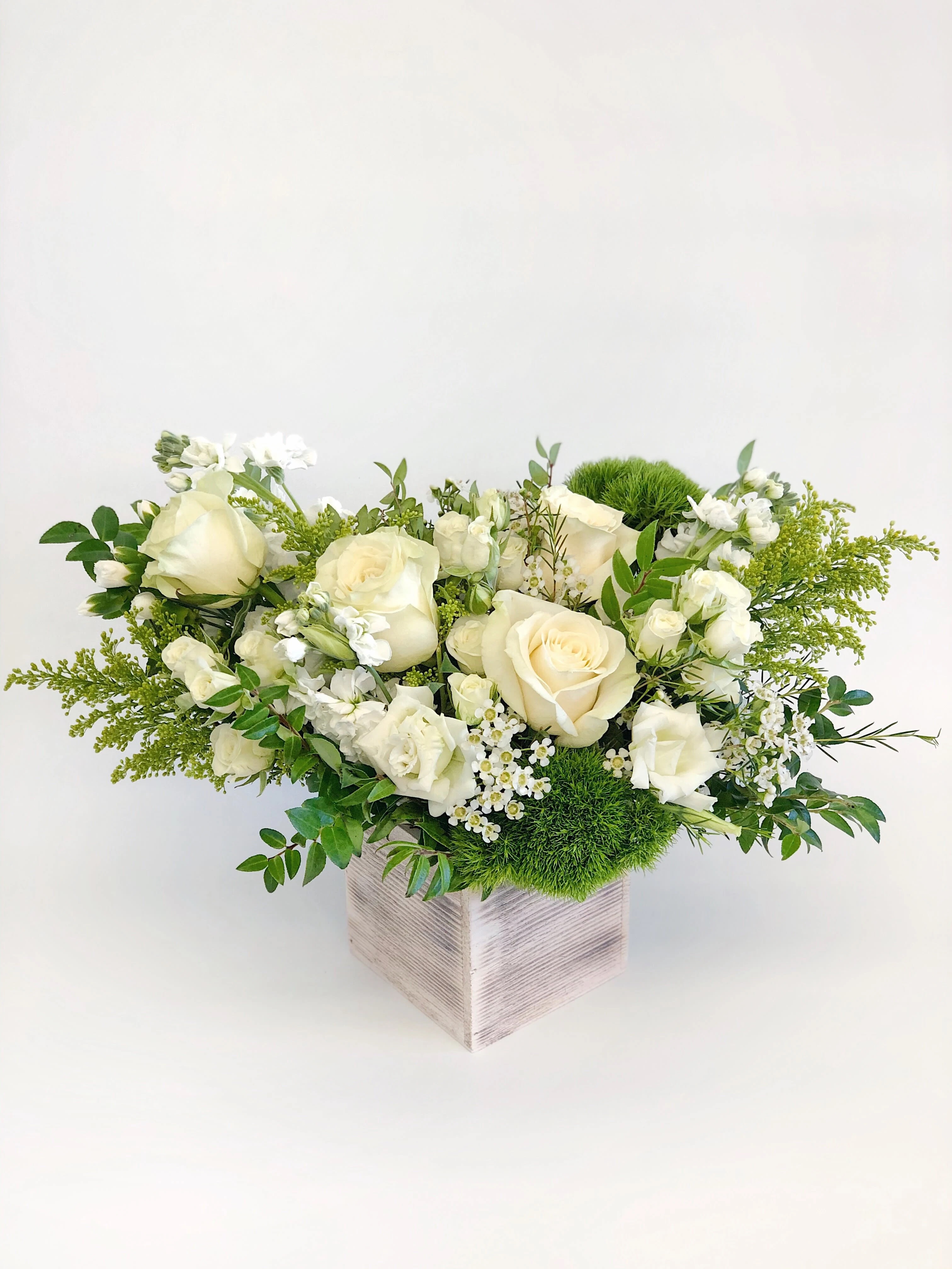 Cream roses and white blooms in a square vase with green accents