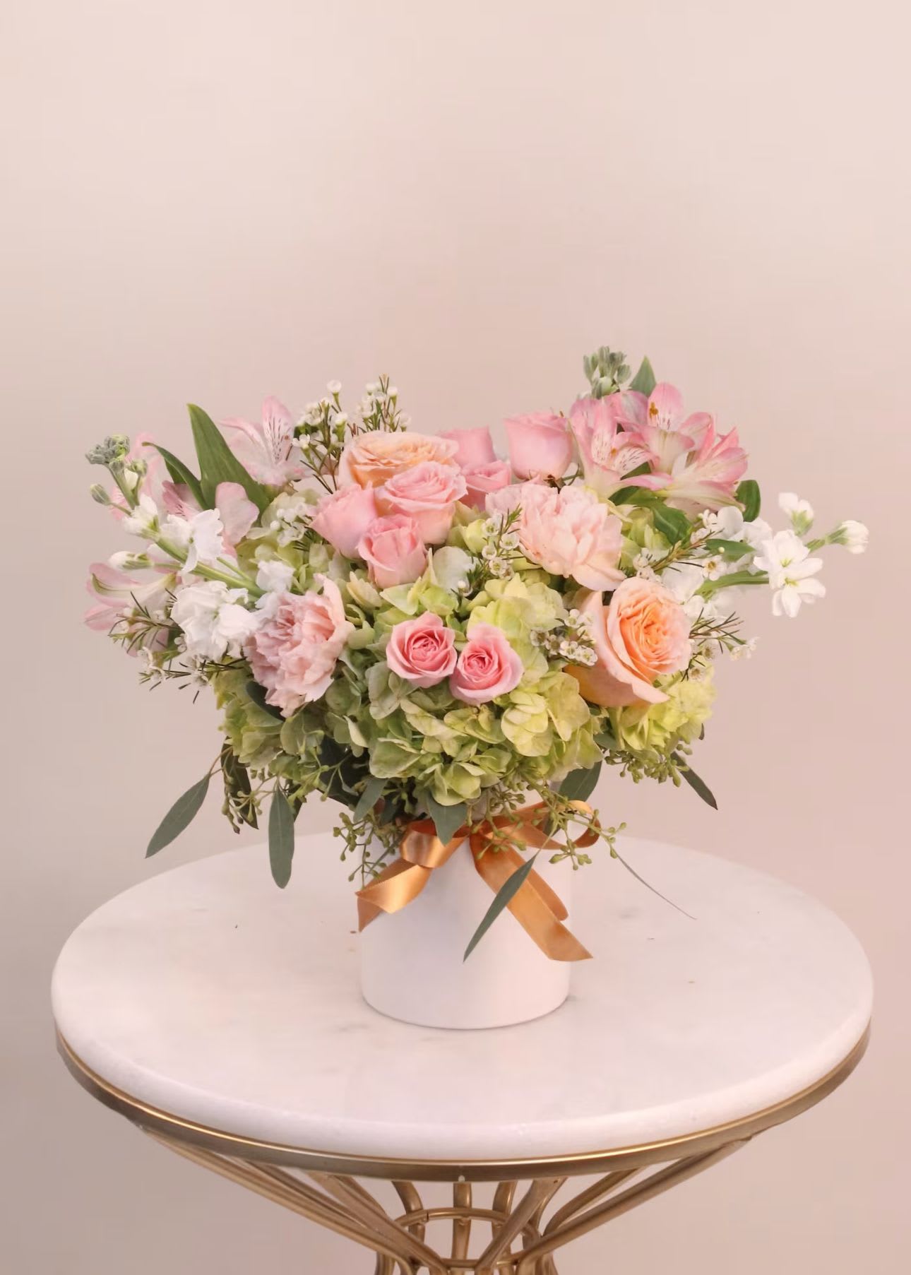 Pink and peach roses arranged with white blooms in a white vase